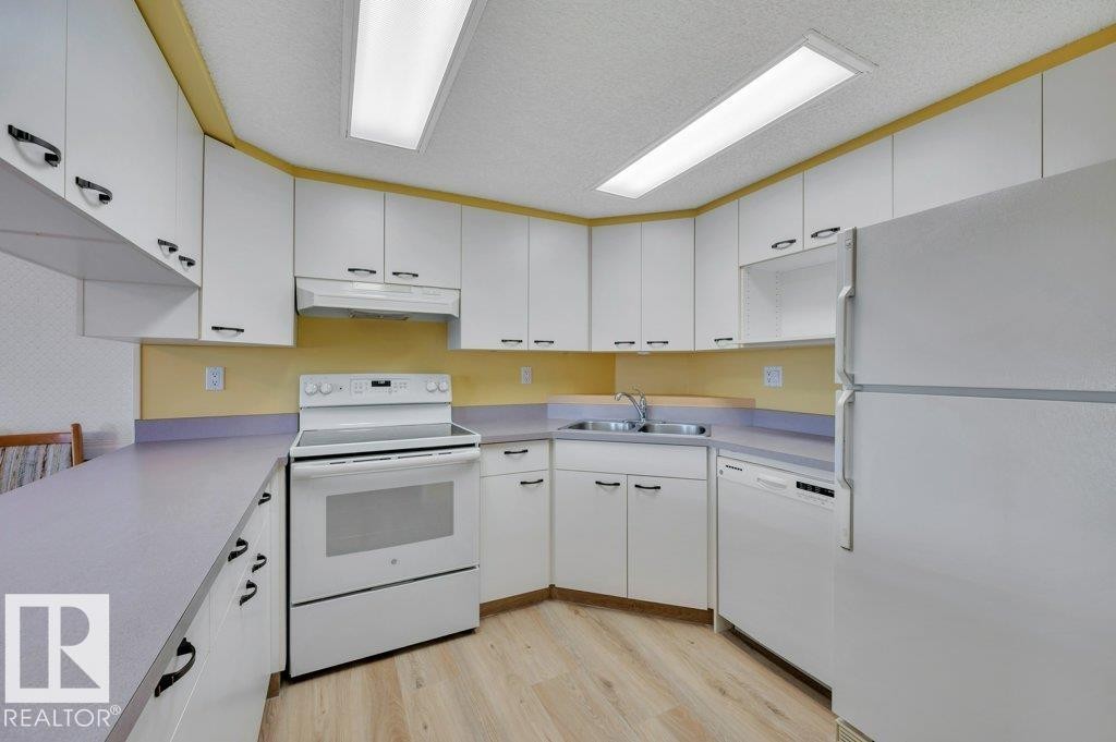 Kitchen featuring extensive white cabinetry, light wood-finish flooring, a double basin sink, and integrated white appliances - 316 2011 137 Avenue, Edmonton, AB - Indoor Photo Showing Kitchen With Double Sink