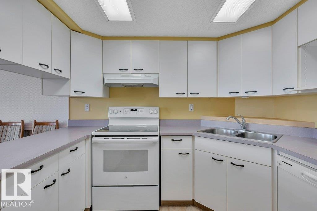 Kitchen featuring white cabinetry with black hardware, a stainless steel double sink, a white electric range, and integrated dishwasher - 316 2011 137 Avenue, Edmonton, AB - Indoor Photo Showing Kitchen With Double Sink