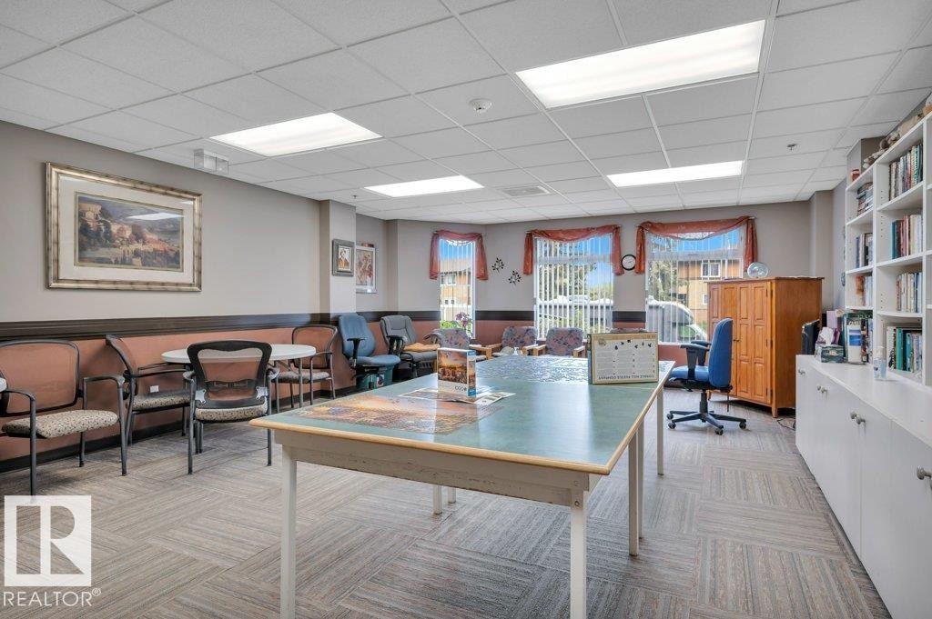 Spacious common room featuring carpet tile flooring, extensive built-in shelving, large window fixtures, and ample natural light - 316 2011 137 Avenue, Edmonton, AB - Indoor