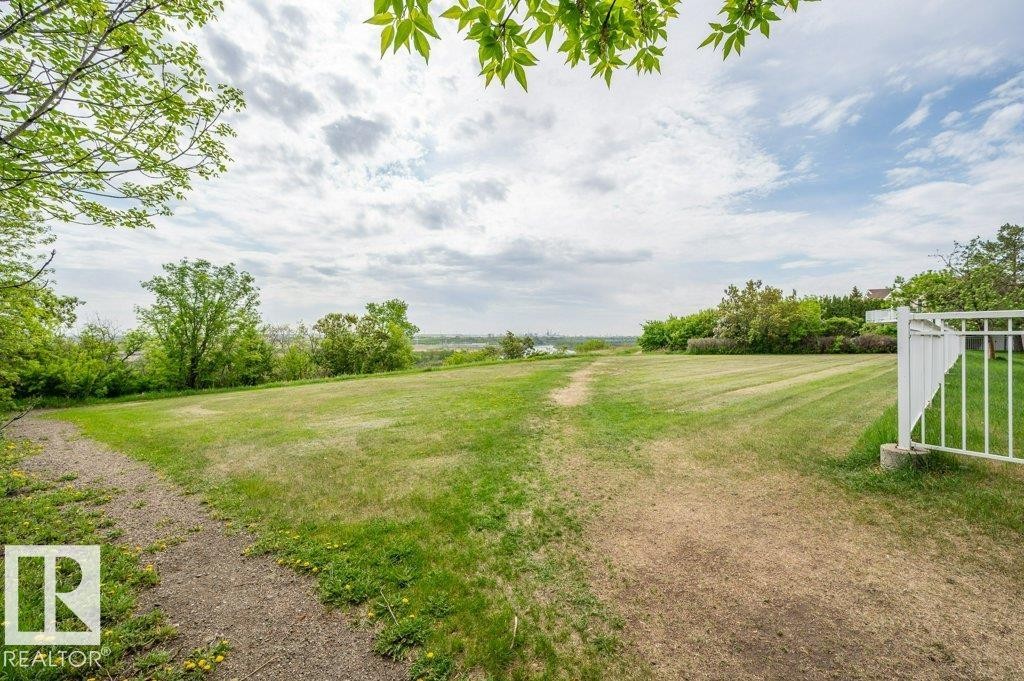 Expansive grassy area featuring a white picket fence, a winding dirt path, and mature trees bordering the property - 316 2011 137 Avenue, Edmonton, AB - Outdoor With View