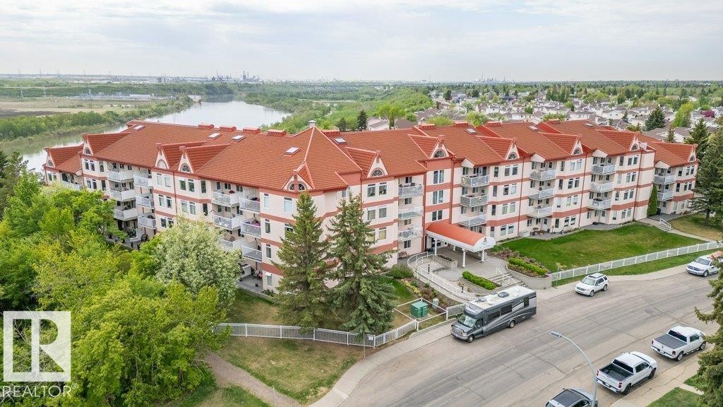 Multi-story residential building featuring a vibrant red roof, numerous balconies, and mature tree landscaping - 316 2011 137 Avenue, Edmonton, AB - Outdoor With Balcony With View
