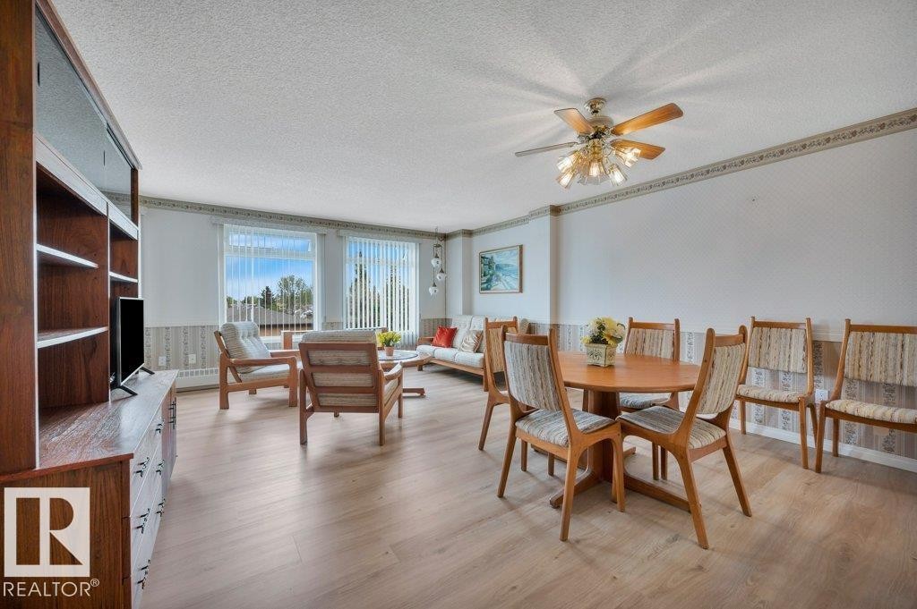 Open-concept living area featuring light wood-finish flooring, multiple windows with vertical blinds, a ceiling fan with integrated lighting, and a built-in wood shelving unit - 316 2011 137 Avenue, Edmonton, AB - Indoor Photo Showing Dining Room