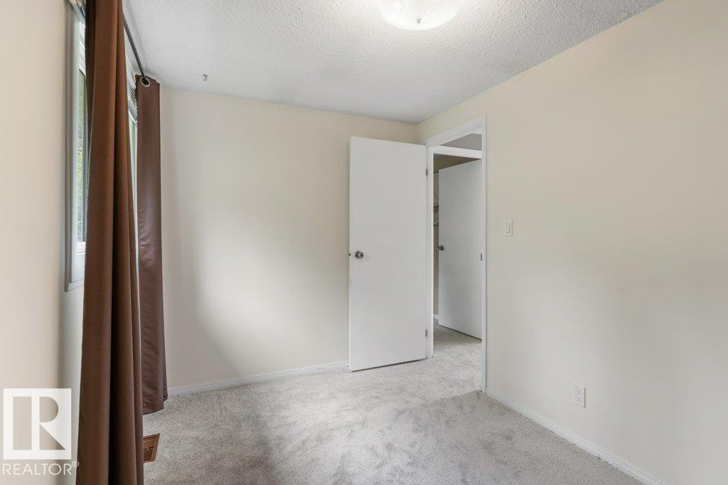 Neutral-toned interior featuring light gray carpeting, white trim, and a window with brown curtains - 171 Ridgewood, St. Albert, AB