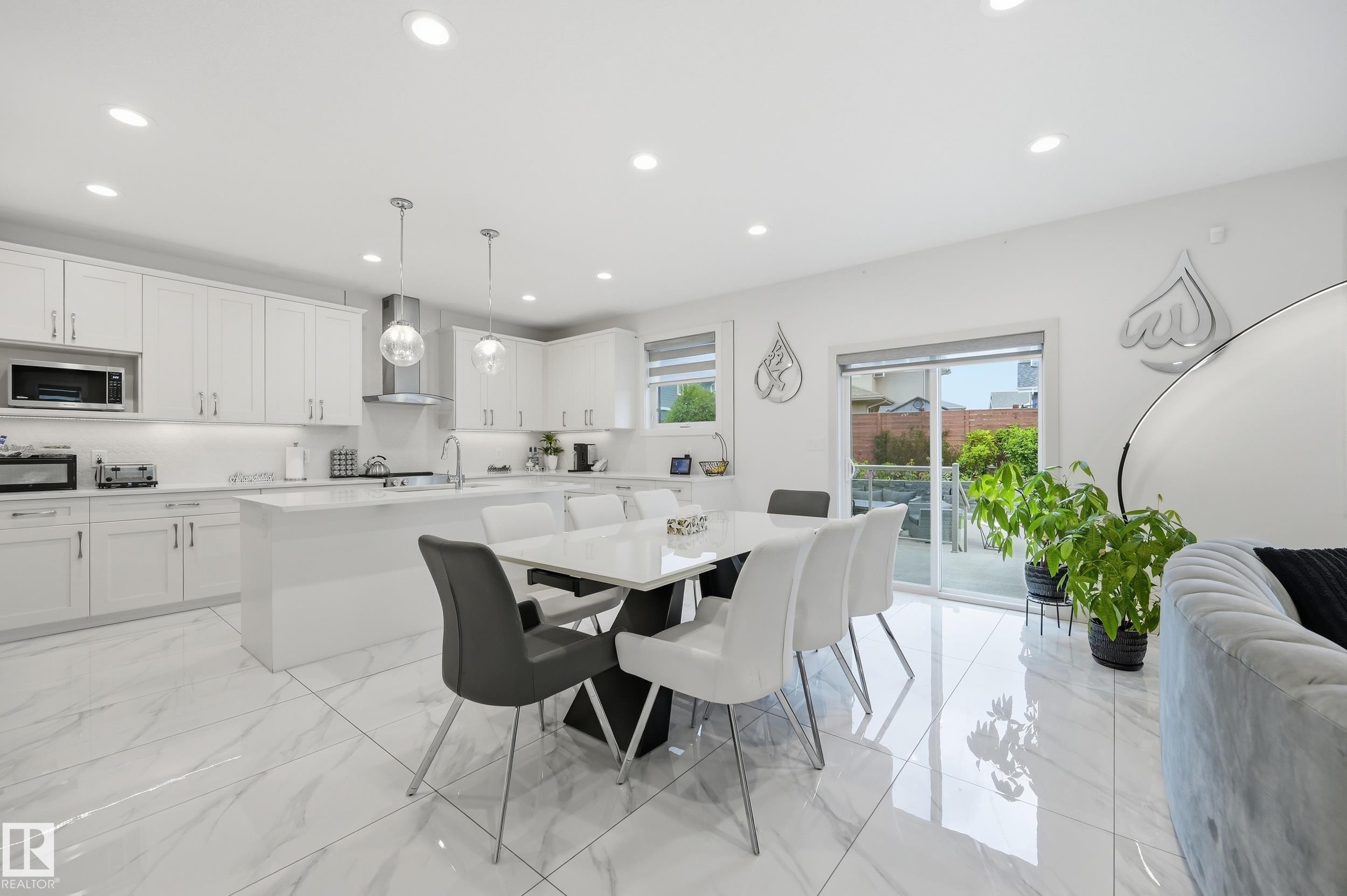 Open-concept kitchen and dining area featuring white shaker cabinetry, an expansive center island, pendant lighting, stainless steel appliances, and large format marble-look tile flooring - 76 Jacobs Close, St. Albert, AB