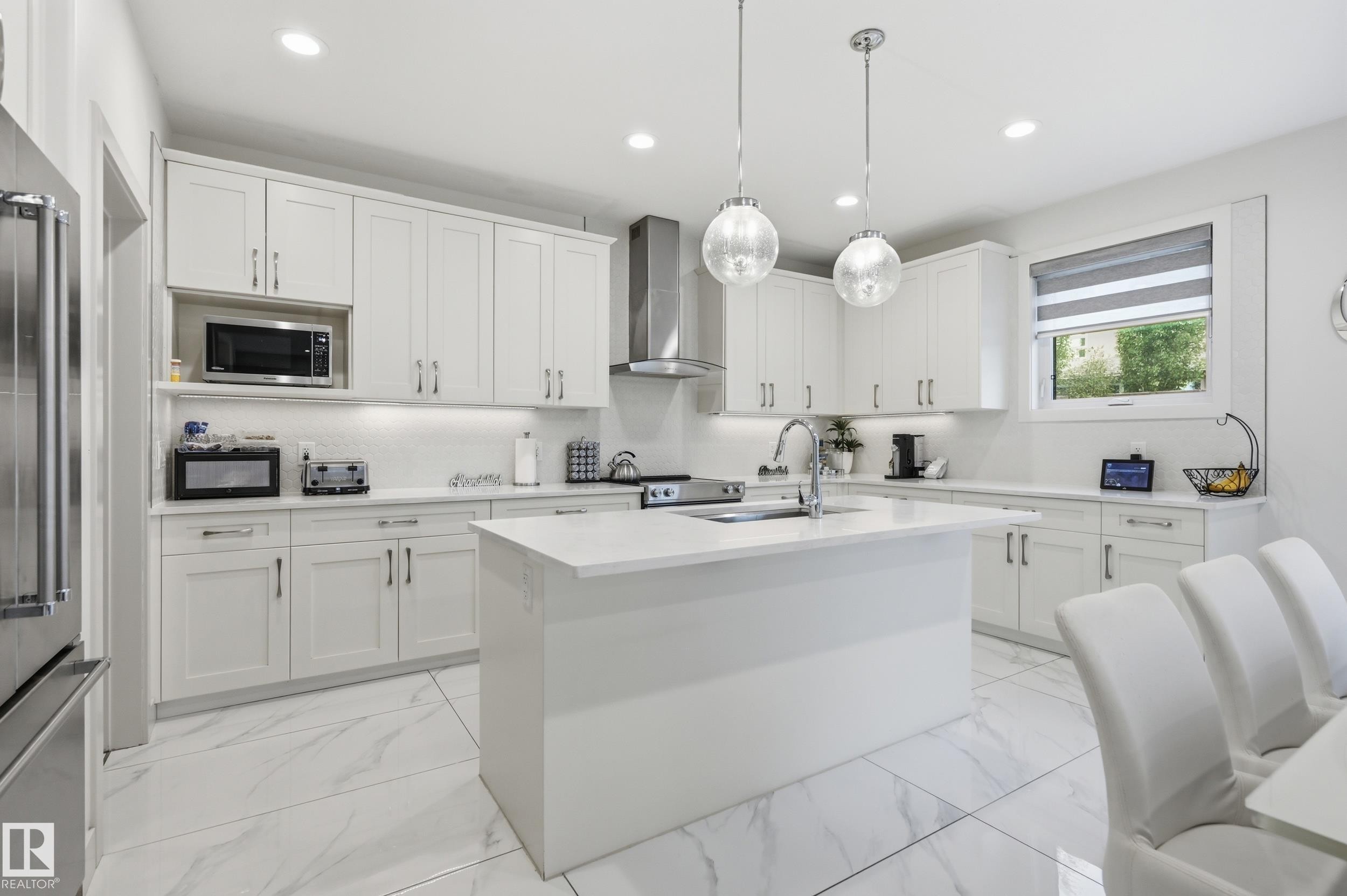 Bright kitchen featuring white shaker cabinetry, an expansive center island with an integrated sink, and stainless steel appliances - 76 Jacobs Close, St. Albert, AB