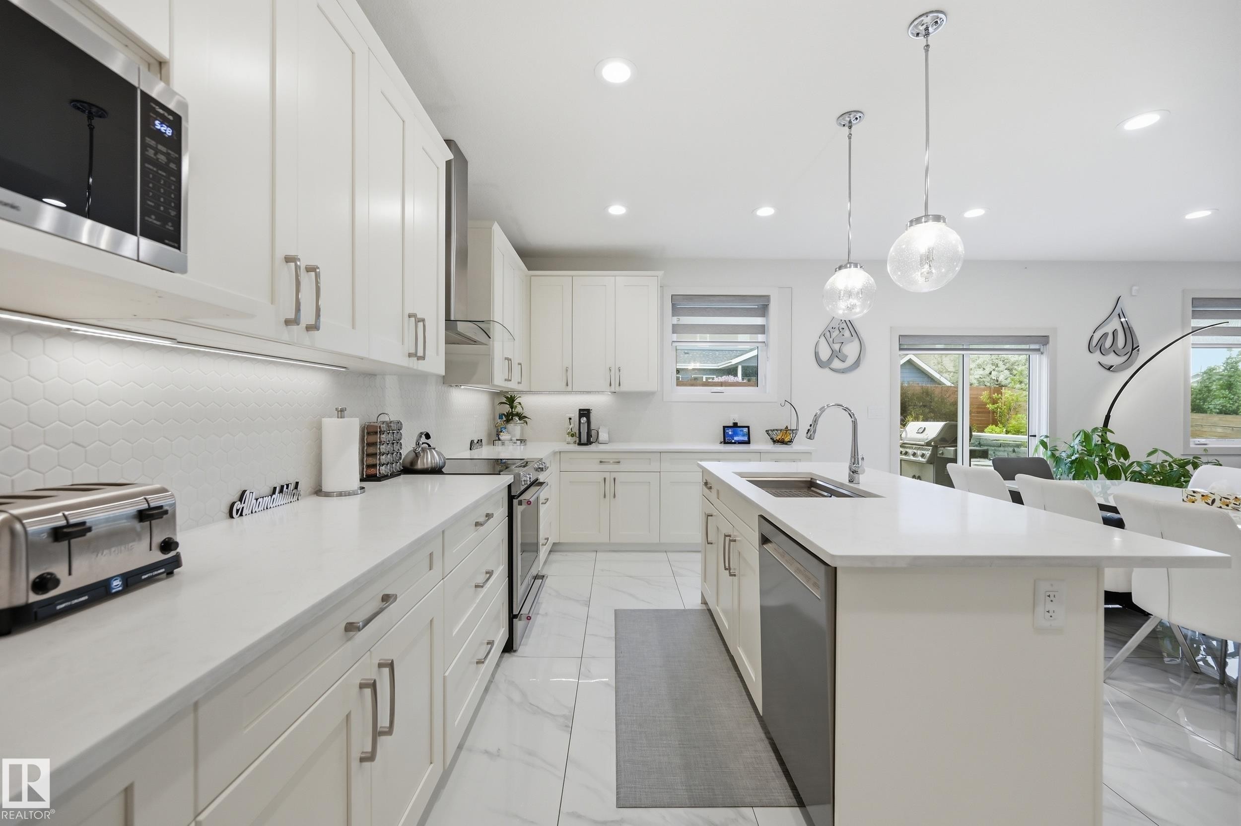 Open-concept kitchen featuring white cabinetry, light countertops, a hexagonal tile backsplash, and stainless steel appliances - 76 Jacobs Close, St. Albert, AB