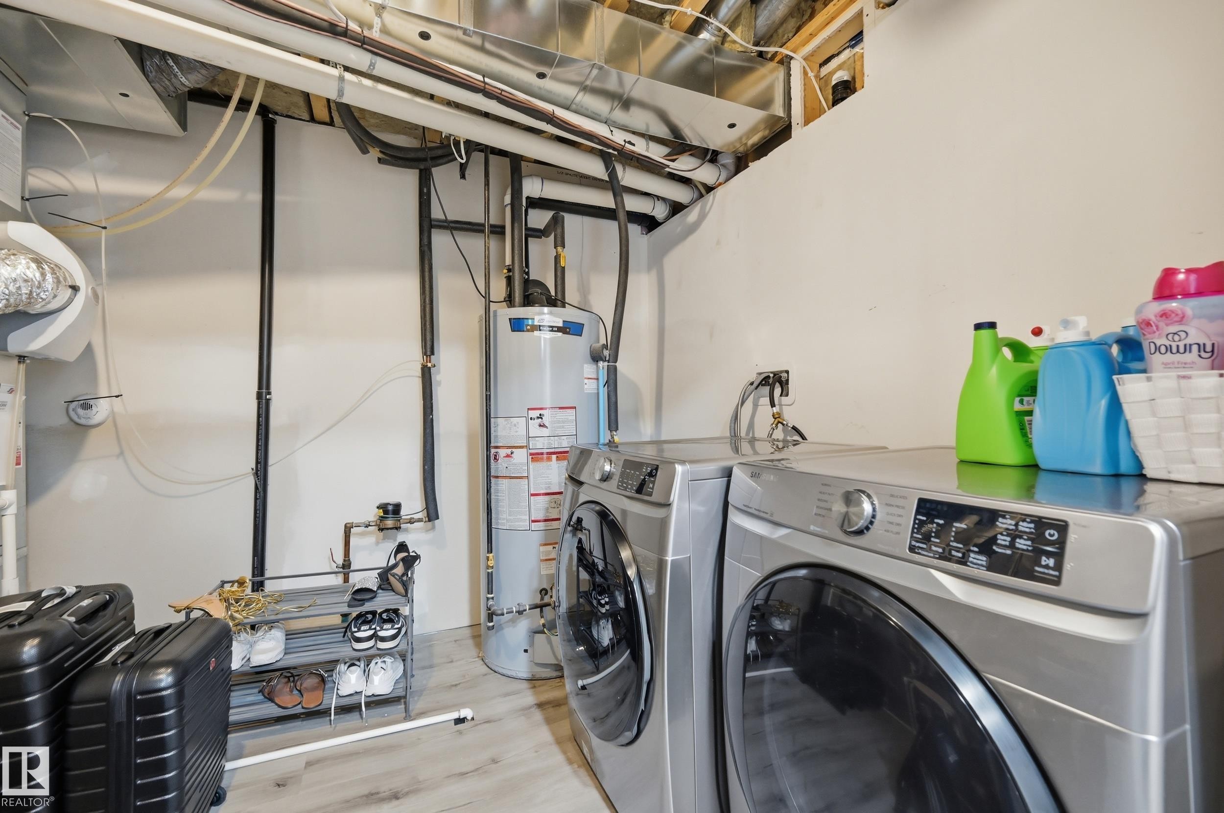 Dedicated laundry area featuring a front-loading washer and dryer set, water heater, exposed utility piping, and light wood-finish flooring - 76 Jacobs Close, St. Albert, AB