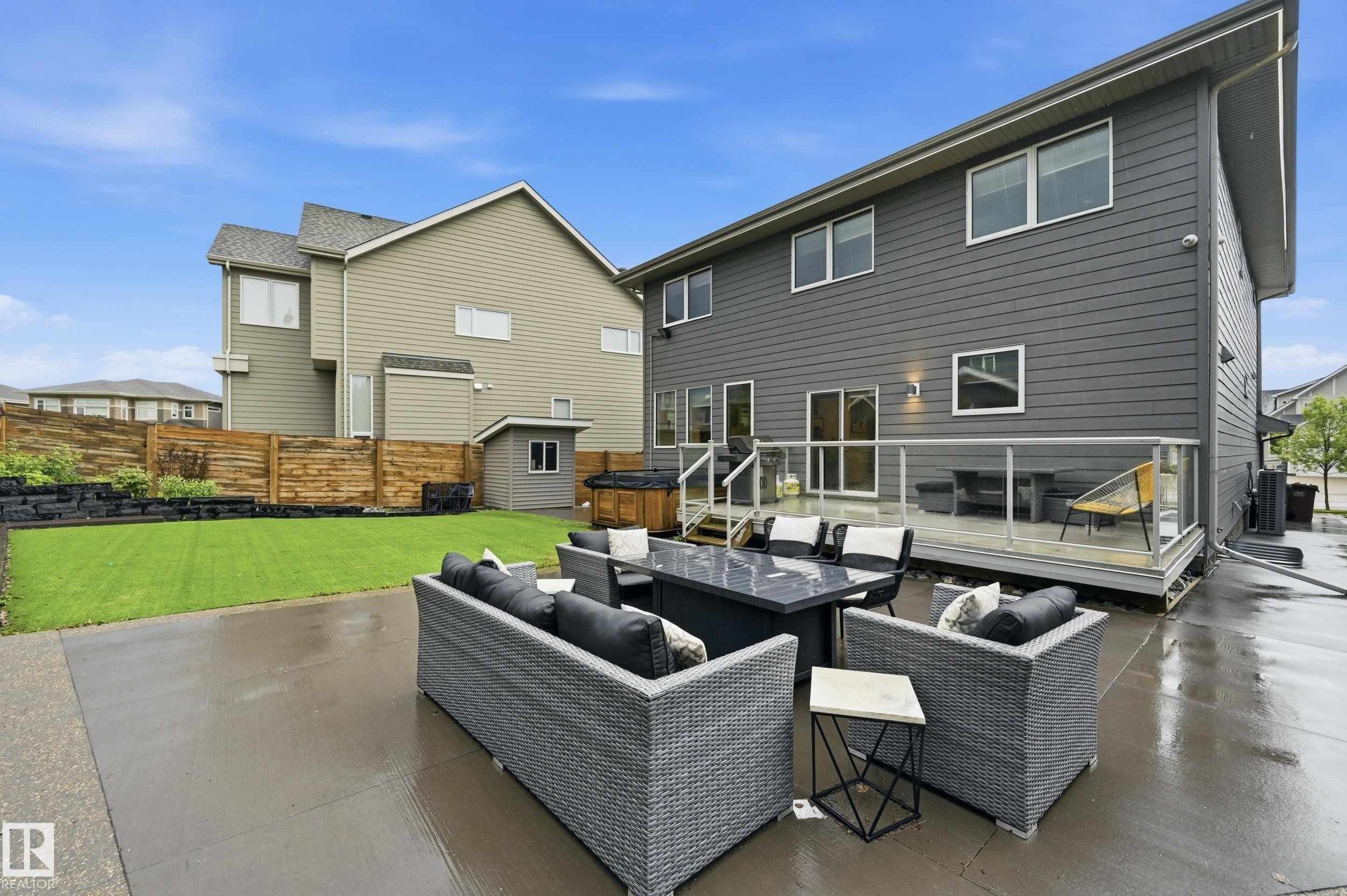 Rear exterior featuring a large concrete patio, expansive manicured lawn, and a multi-level wood deck with glass panel railing - 76 Jacobs Close, St. Albert, AB