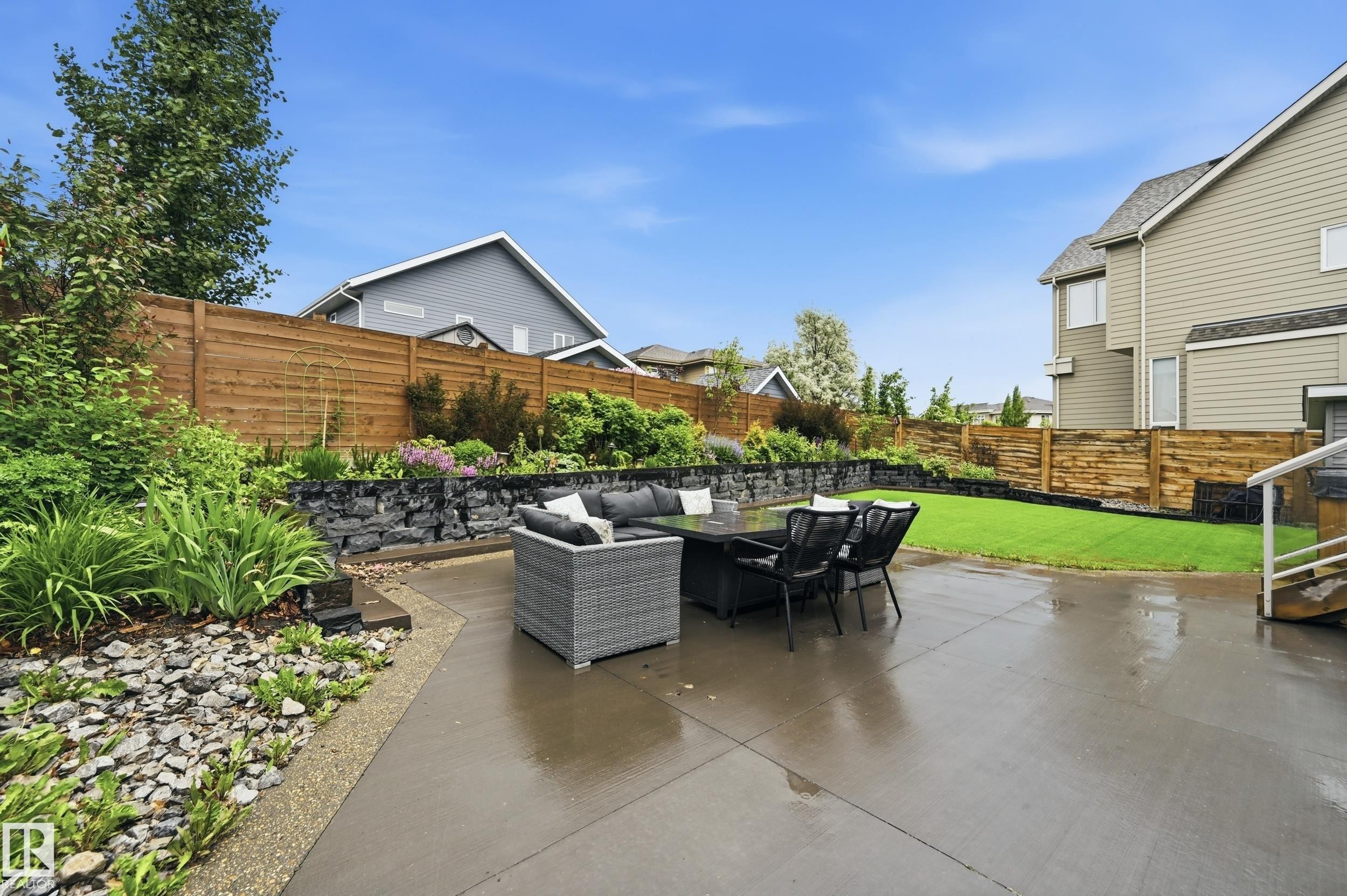 Expansive concrete patio area with a stone retaining wall and lush landscaping - 76 Jacobs Close, St. Albert, AB