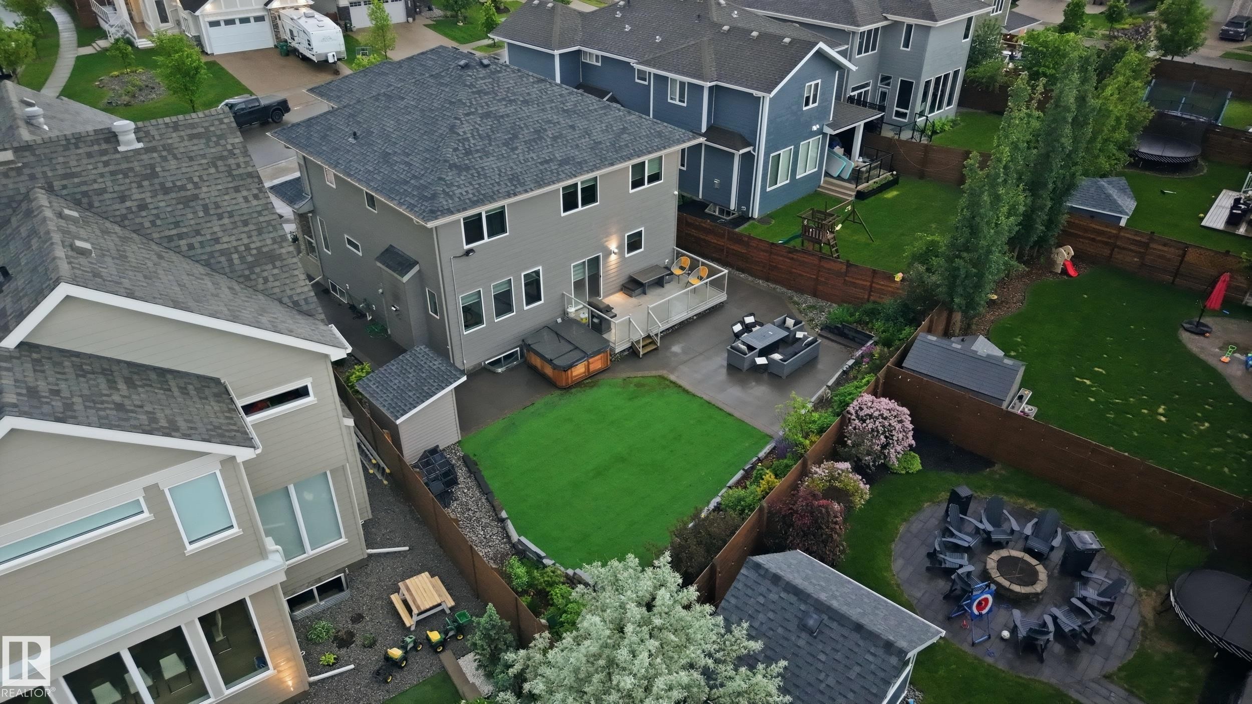 Rear exterior featuring a spacious composite deck, a hot tub, a paved patio, and a manicured lawn - 76 Jacobs Close, St. Albert, AB