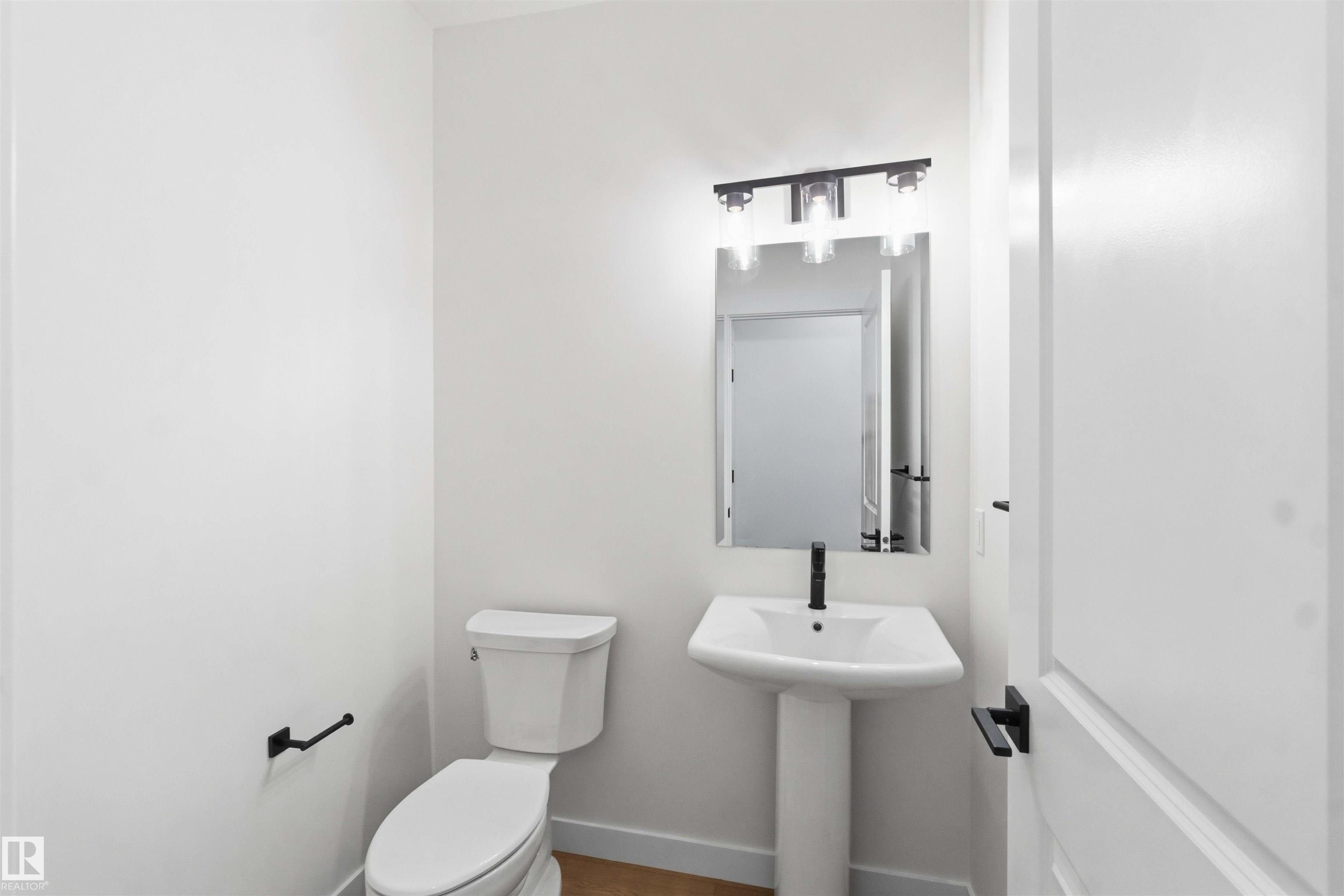 Pedestal sink with matte black faucet, wall-mounted mirror, and contemporary light fixture - 1085 Cristall Crescent Sw, Edmonton, AB - Indoor Photo Showing Bathroom
