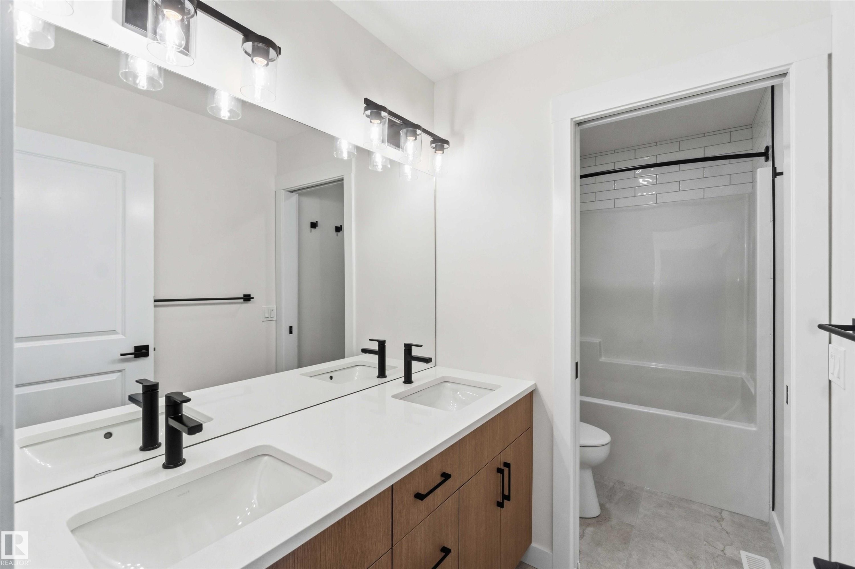 Bathroom featuring a double vanity with white countertops, integrated sinks, and matte black fixtures - 1085 Cristall Crescent Sw, Edmonton, AB - Indoor Photo Showing Bathroom
