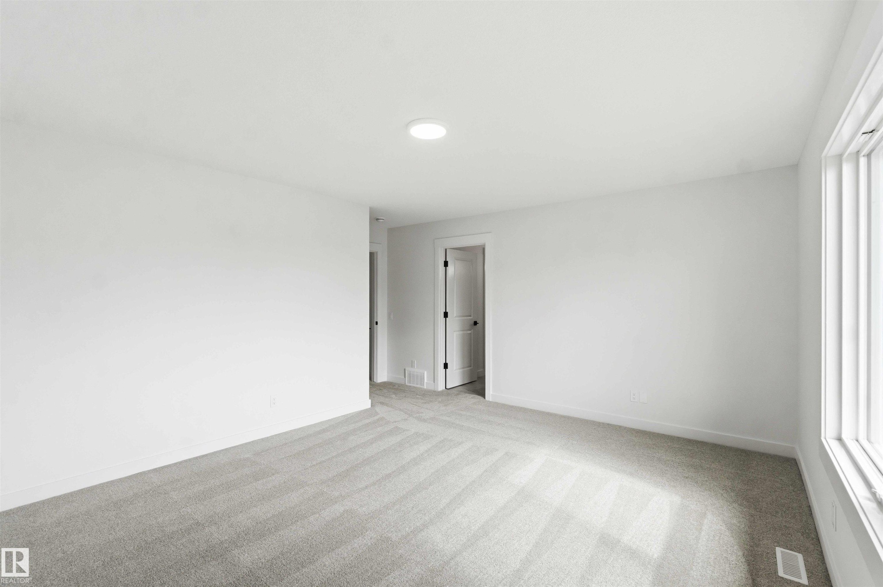Spacious room featuring light gray carpeting, neutral wall finishes, a large window, a recessed ceiling light, and a white interior door with dark hardware - 1085 Cristall Crescent Sw, Edmonton, AB - Indoor Photo Showing Other Room