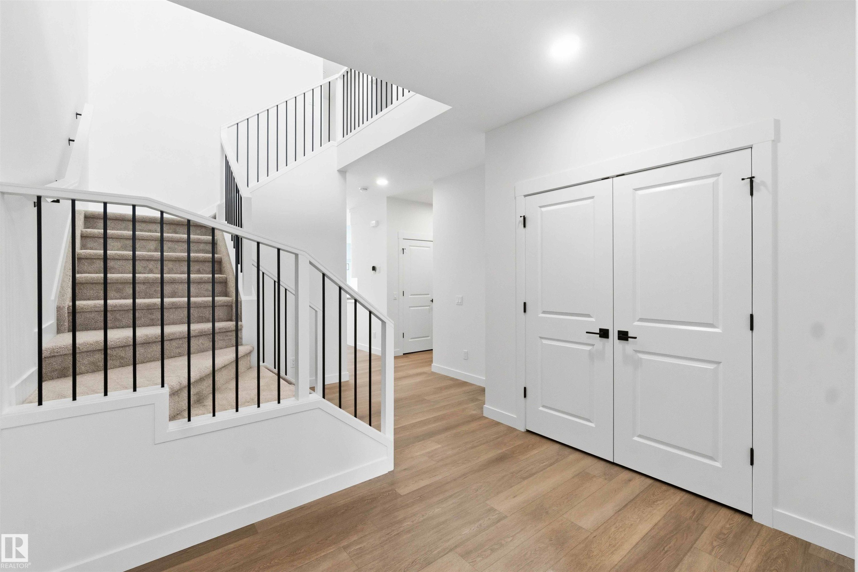 Two-story foyer featuring contemporary black metal balusters, light wood-finish flooring, recessed lighting, and white paneled doors with matte black hardware - 1085 Cristall Crescent Sw, Edmonton, AB - Indoor Photo Showing Other Room