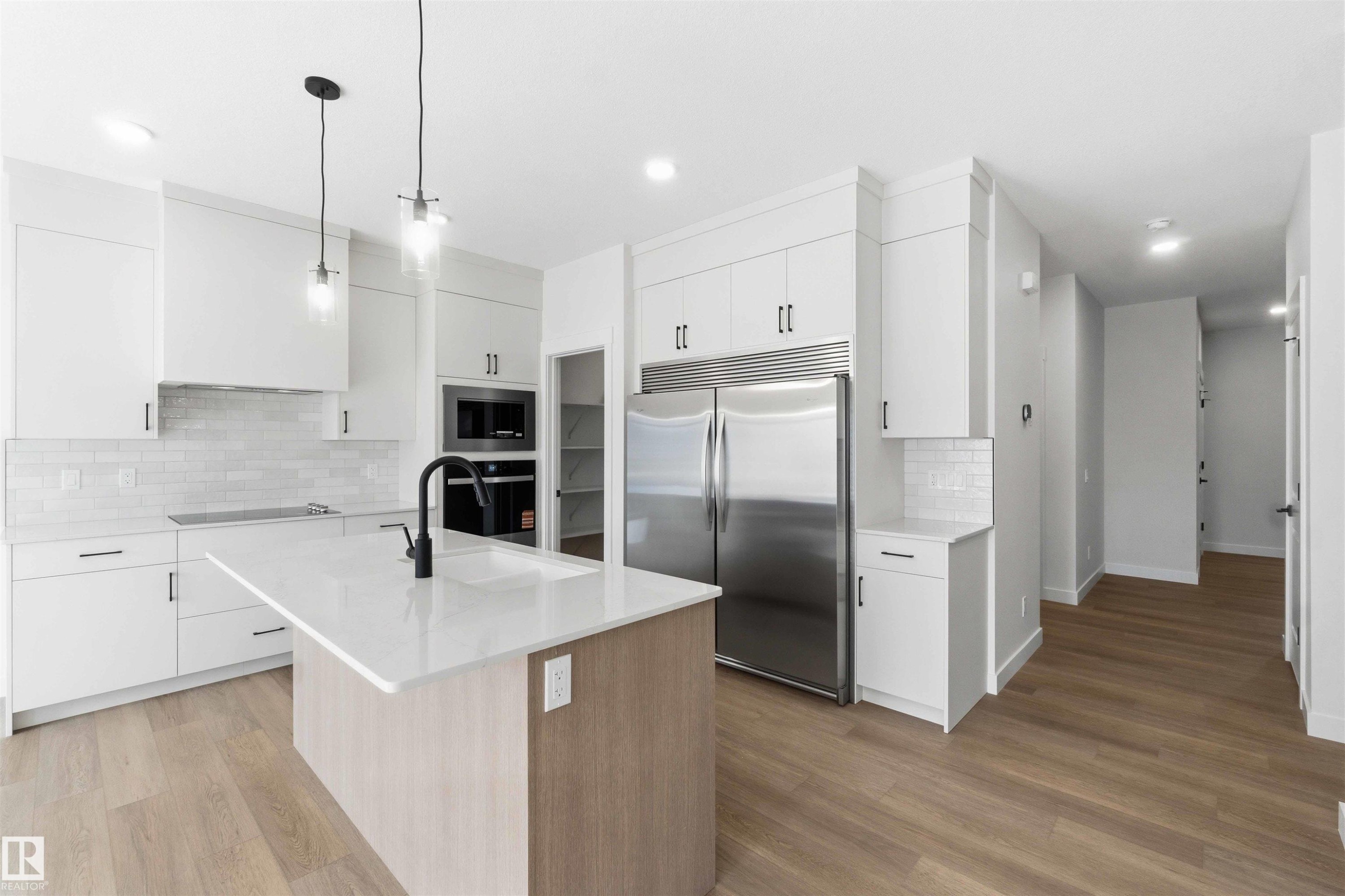 Modern kitchen featuring white cabinetry, a large center island with a quartz countertop, stainless steel appliances, and wood-finish flooring - 1085 Cristall Crescent Sw, Edmonton, AB - Indoor Photo Showing Kitchen With Upgraded Kitchen