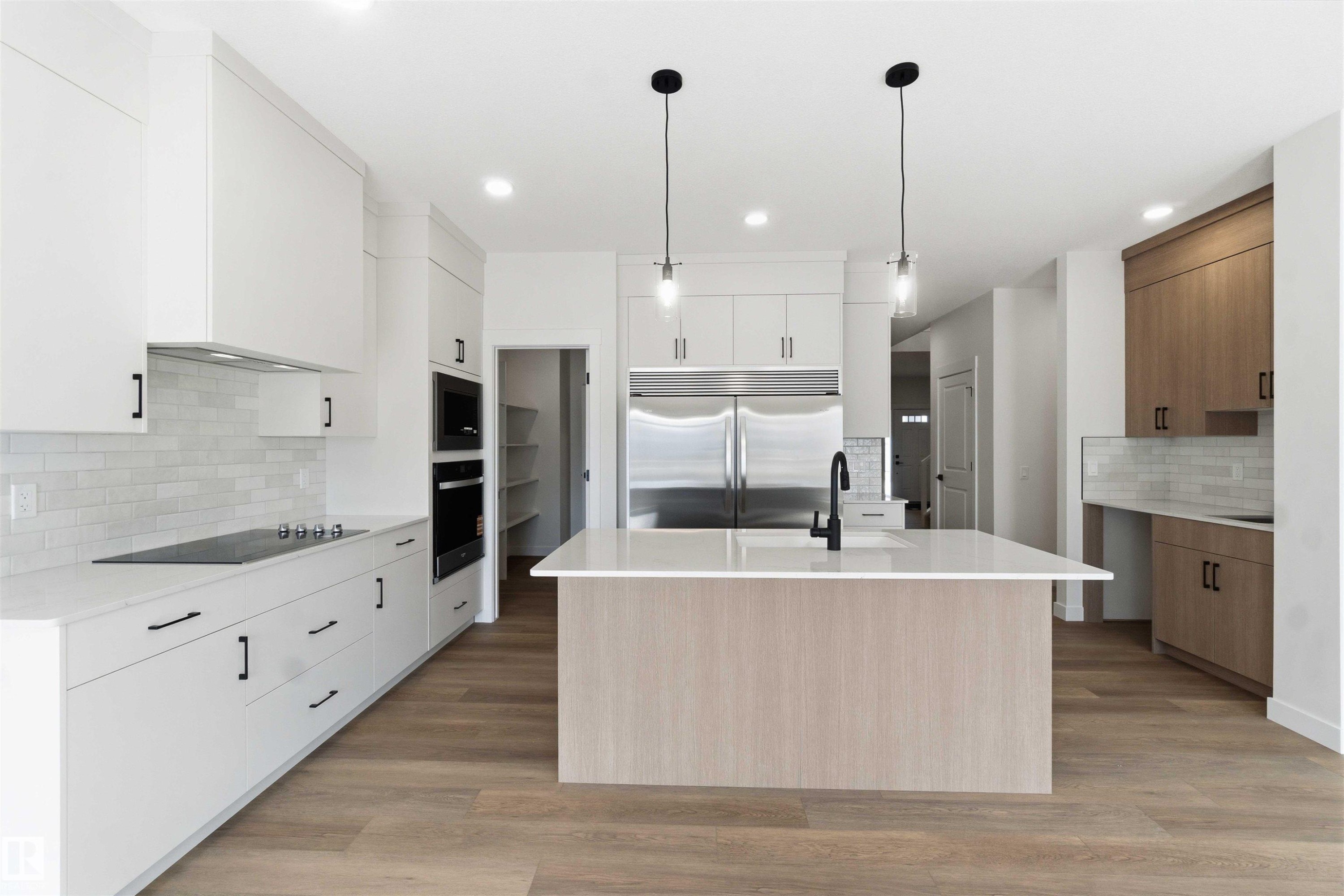 Modern kitchen featuring a central island with a waterfall countertop, integrated stainless steel appliances, wood-finish flooring, a white subway tile backsplash, and recessed lighting - 1085 Cristall Crescent Sw, Edmonton, AB - Indoor Photo Showing Kitchen With Upgraded Kitchen