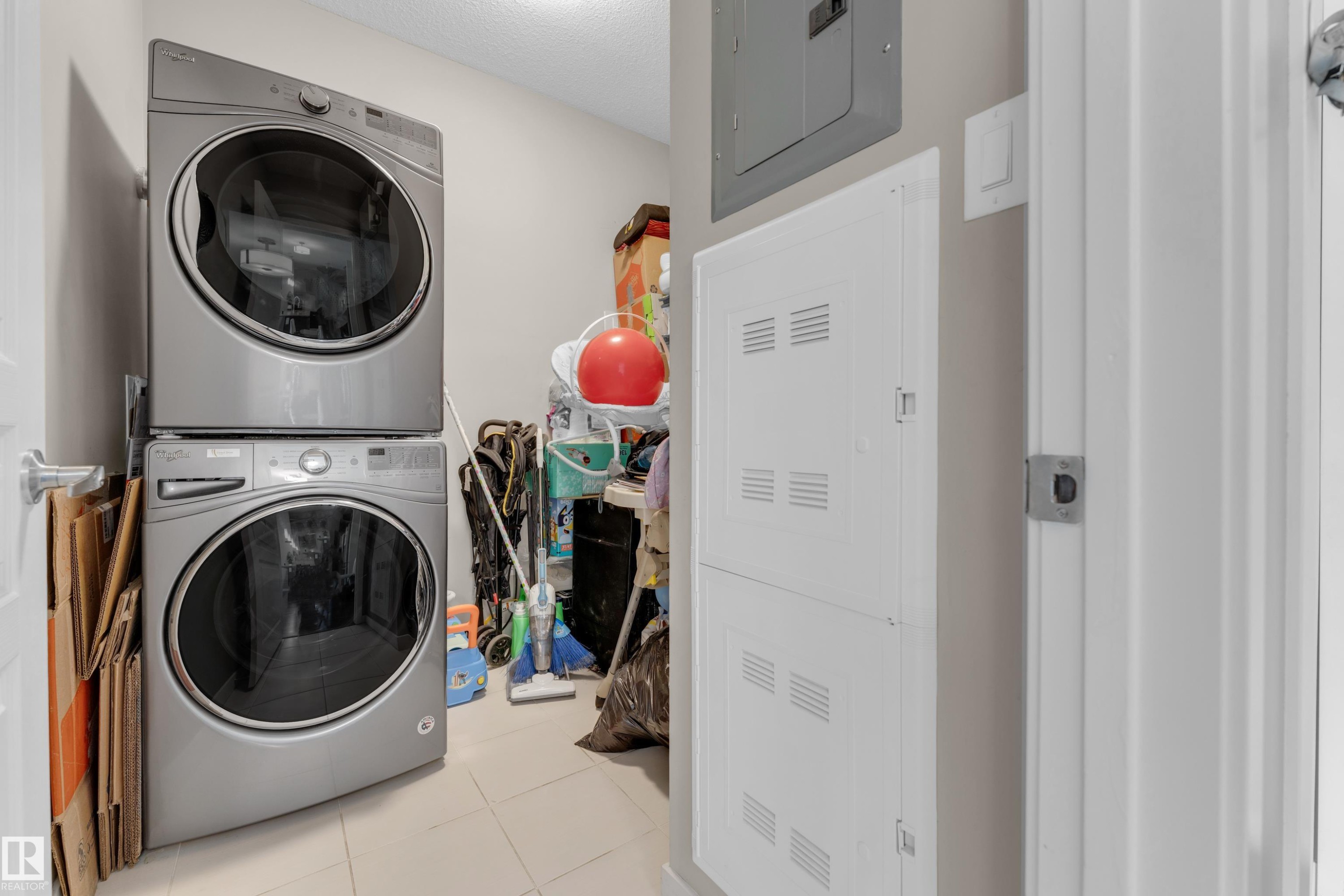 Utility area featuring stacked laundry appliances, tiled flooring, and neutral wall paint - 115 812 Welsh Drive Sw, Edmonton, AB