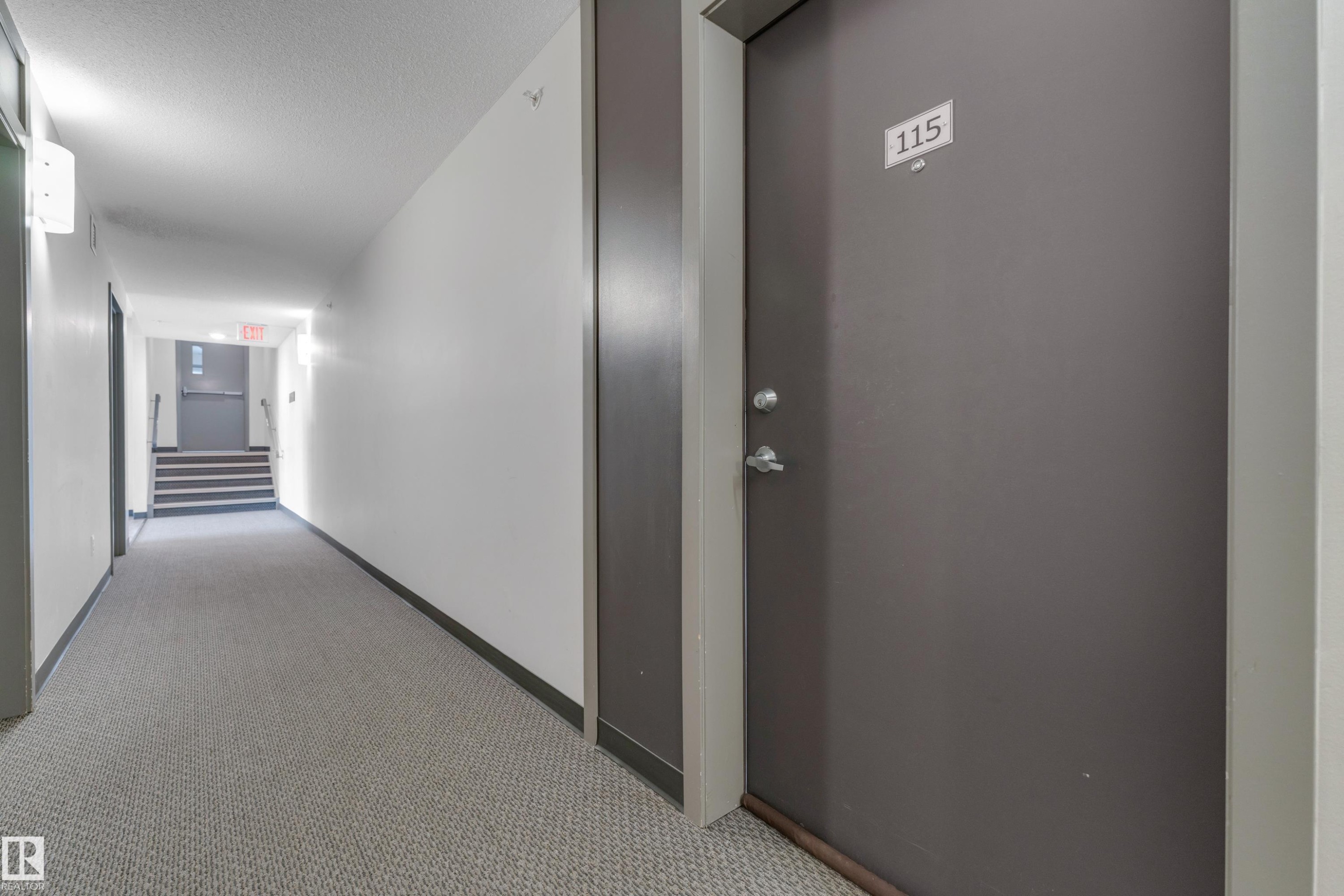 Property entrance featuring a solid door with modern hardware, leading to a hallway with patterned carpeting - 115 812 Welsh Drive Sw, Edmonton, AB