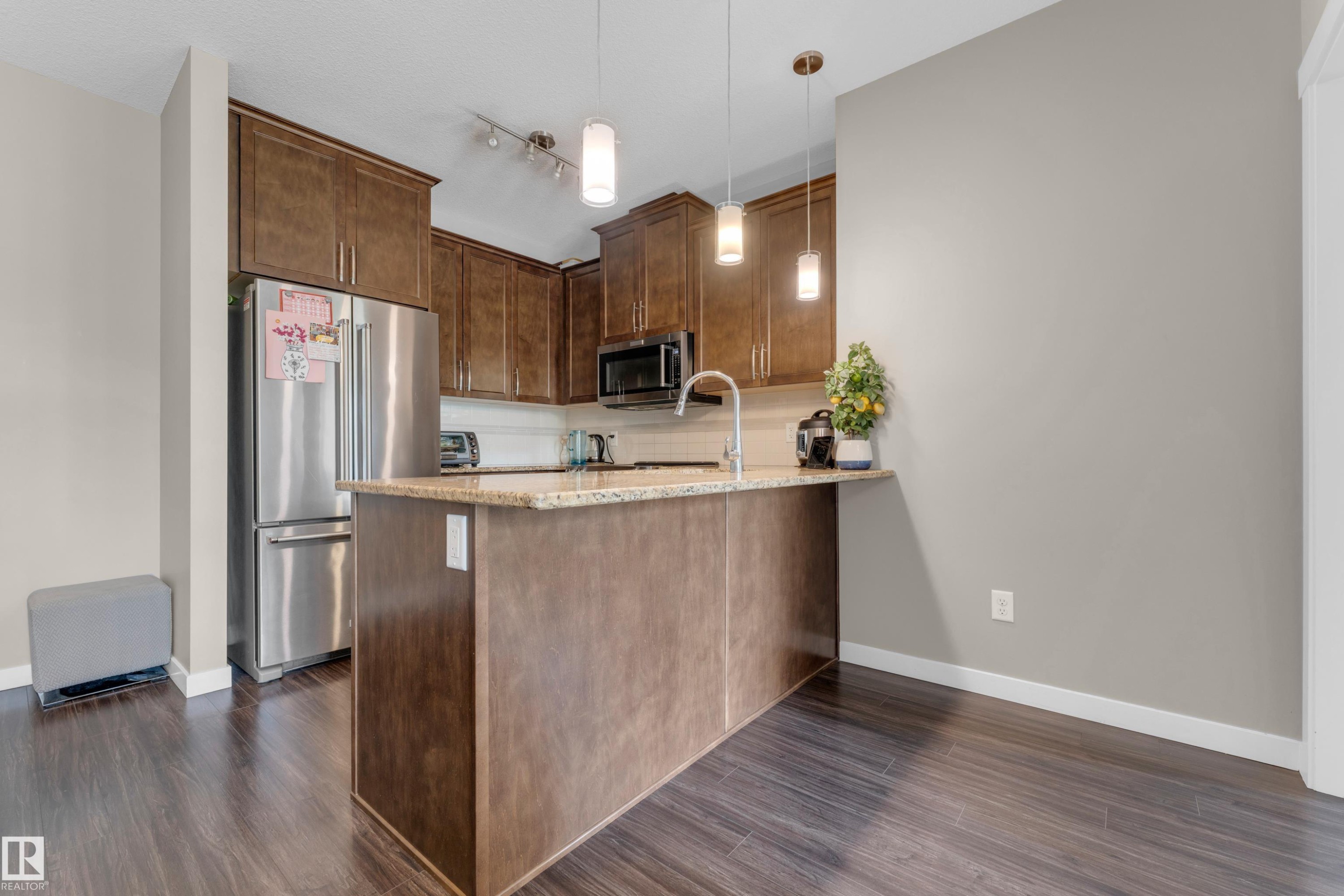 Kitchen featuring wood-finish cabinetry, stainless steel appliances, a center island with pendant lighting, a gooseneck faucet, and light-toned countertops - 115 812 Welsh Drive Sw, Edmonton, AB