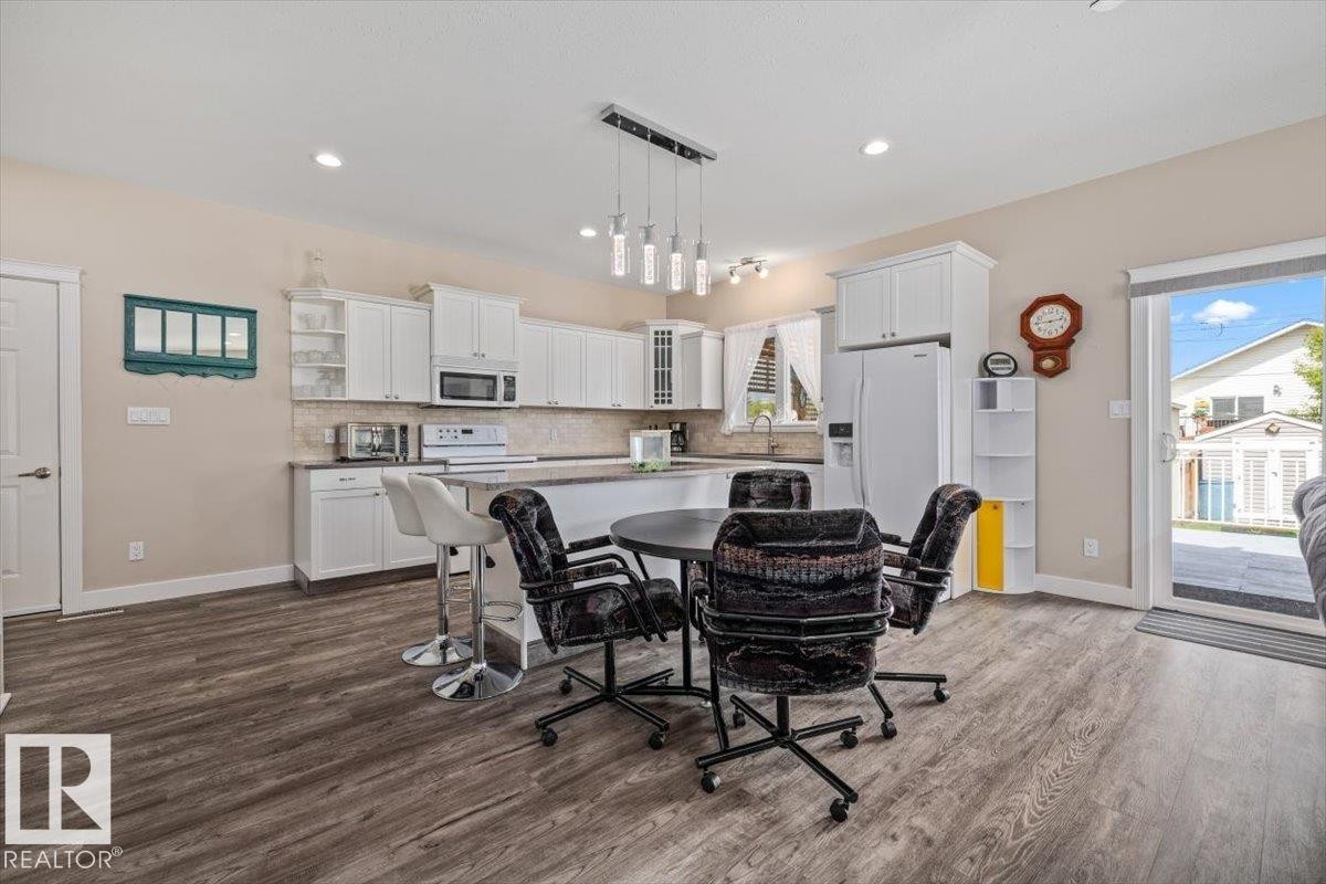 Open-concept kitchen and dining area featuring wood-finish flooring, white cabinetry, and a neutral backsplash - 4708 47A Avenue, Onoway, AB
