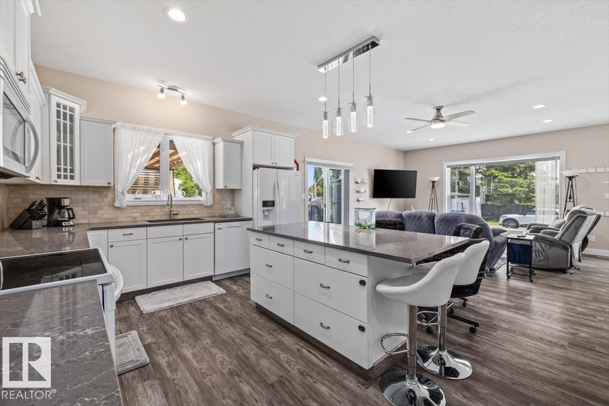Open-concept kitchen featuring white cabinetry, stone-finish countertops, and a subway tile backsplash - 4708 47A Avenue, Onoway, AB