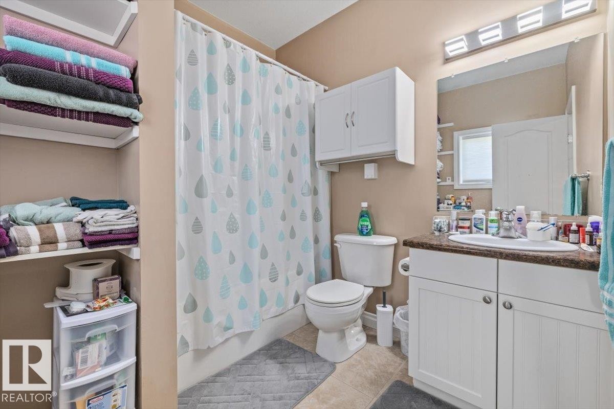 Bathroom featuring a single vanity with a laminate countertop, a mirrored medicine cabinet, a full bathtub with shower, and built-in shelving - 4708 47A Avenue, Onoway, AB