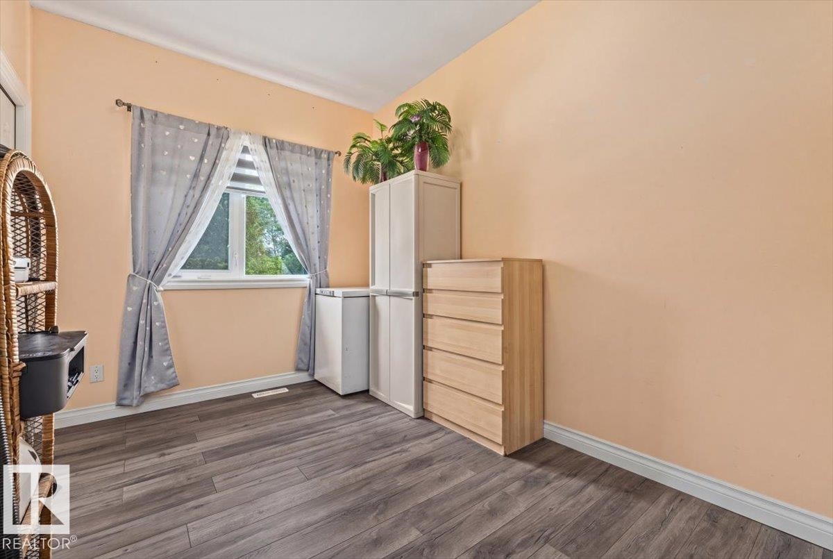 Bedroom featuring a single window with blinds, wood-finish flooring, and light-colored walls - 4708 47A Avenue, Onoway, AB