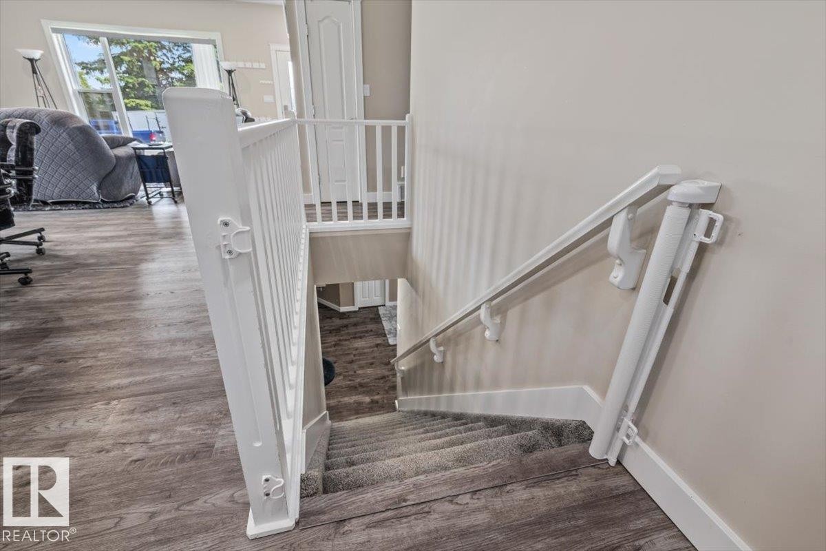 Interior staircase featuring carpeted treads, white railing, and a wall-mounted handrail - 4708 47A Avenue, Onoway, AB