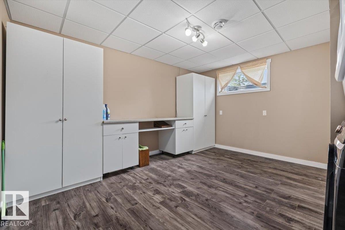 Dedicated utility space featuring extensive built-in white cabinetry, a built-in countertop with open shelving, wood-finish flooring, and a drop ceiling with recessed lighting - 4708 47A Avenue, Onoway, AB