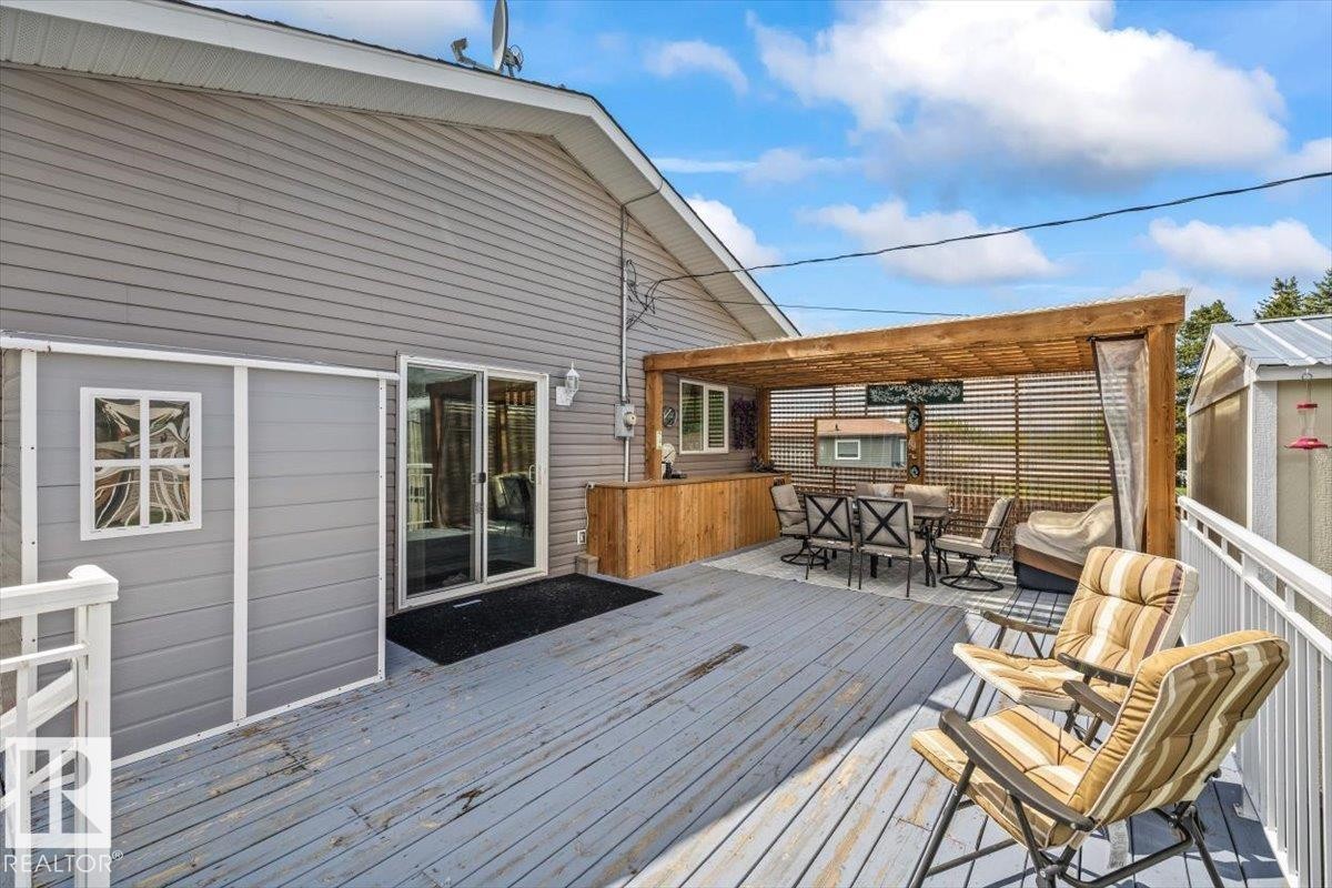 Expansive outdoor deck featuring a wooden pergola, privacy screen, built-in wooden bar, and direct access to interior spaces via sliding glass doors - 4708 47A Avenue, Onoway, AB