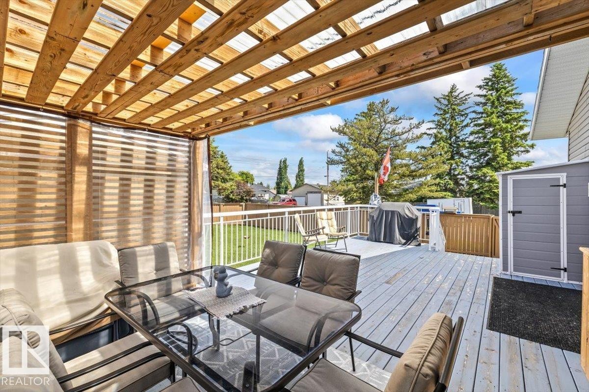 Expansive outdoor deck featuring a wood pergola with a translucent roof, white railings, and a detached gray storage shed - 4708 47A Avenue, Onoway, AB