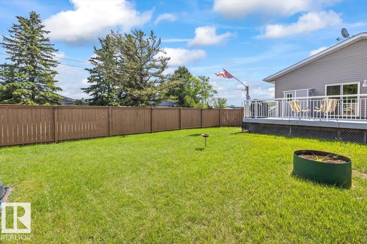 Expansive grassy yard featuring a wood fence, a raised deck with white railings, and a siding exterior - 4708 47A Avenue, Onoway, AB