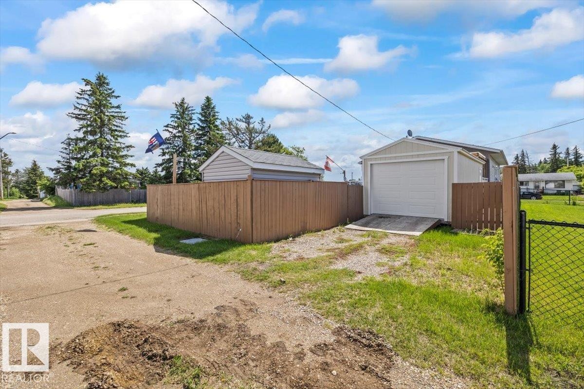 Detached garage with a white overhead door and siding, set behind a wooden fence - 4708 47A Avenue, Onoway, AB