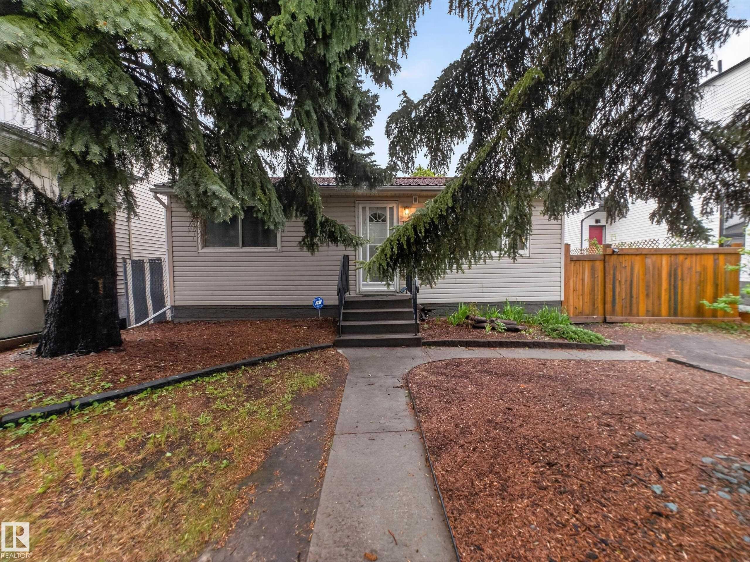 Single-story exterior with light-colored siding, a dark metal roof, and a concrete walkway leading to the entrance - 10809 150 Street, Edmonton, AB