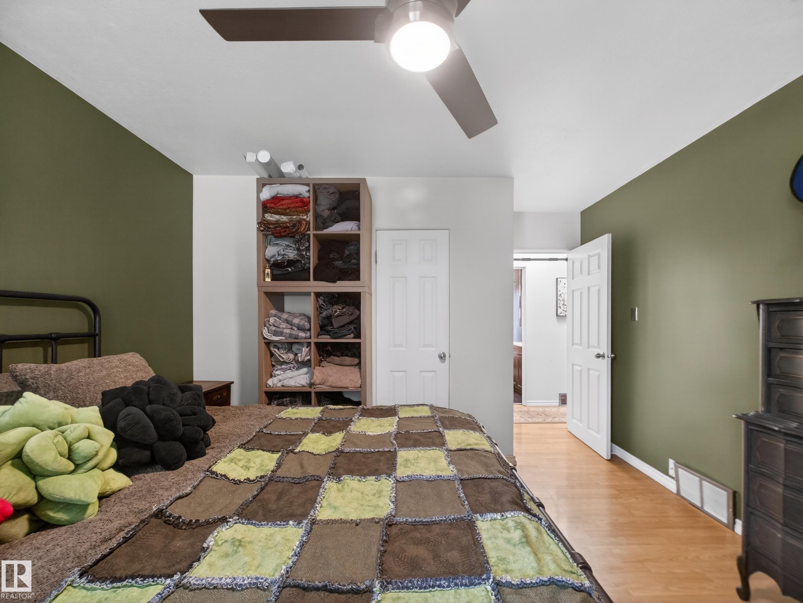 Bedroom featuring a ceiling fan with integrated lighting, wood-finish flooring, and a multi-toned accent wall - 10809 150 Street, Edmonton, AB