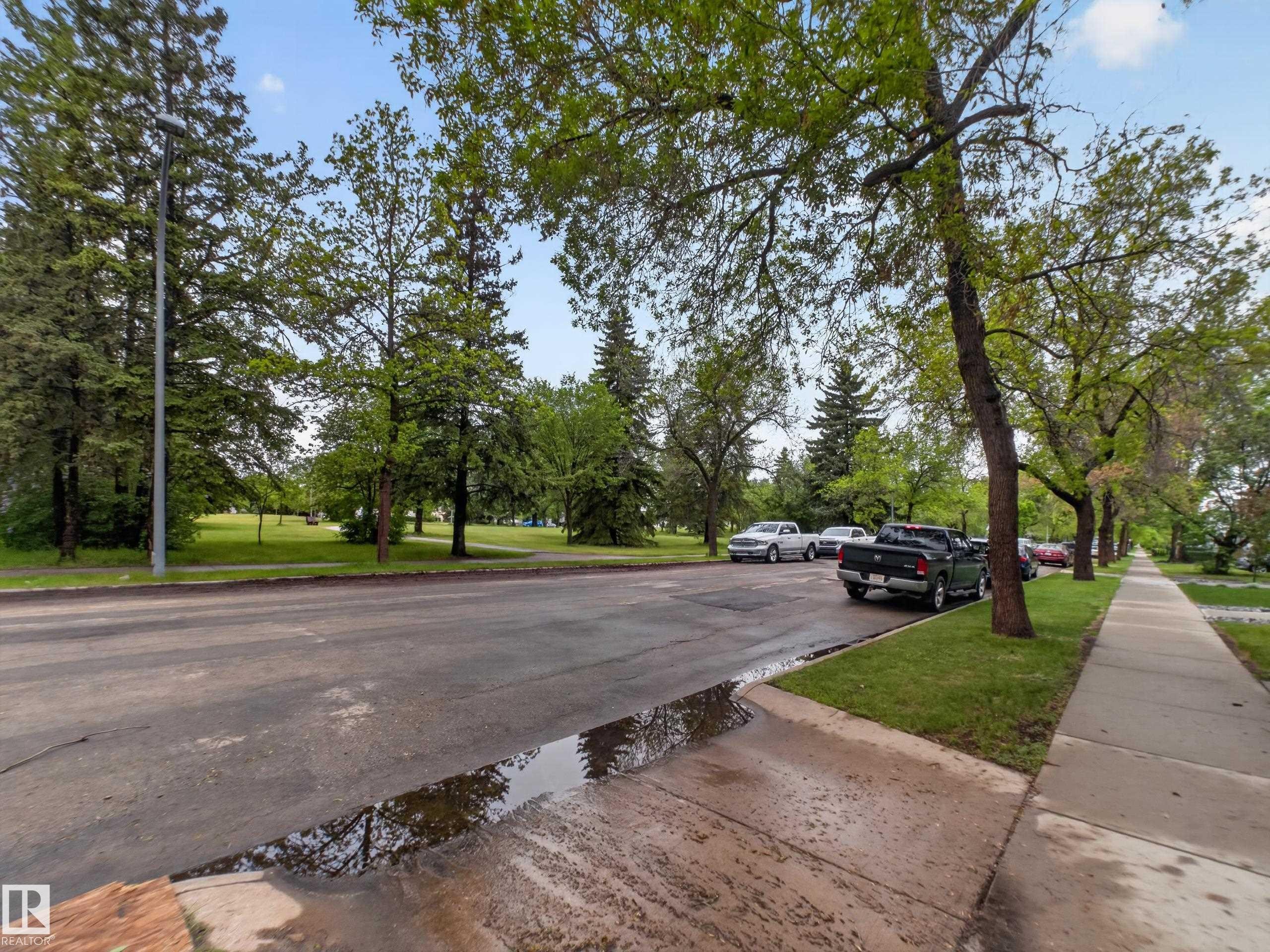 Street-level perspective featuring mature trees, paved sidewalk, and a manicured green space - 10809 150 Street, Edmonton, AB