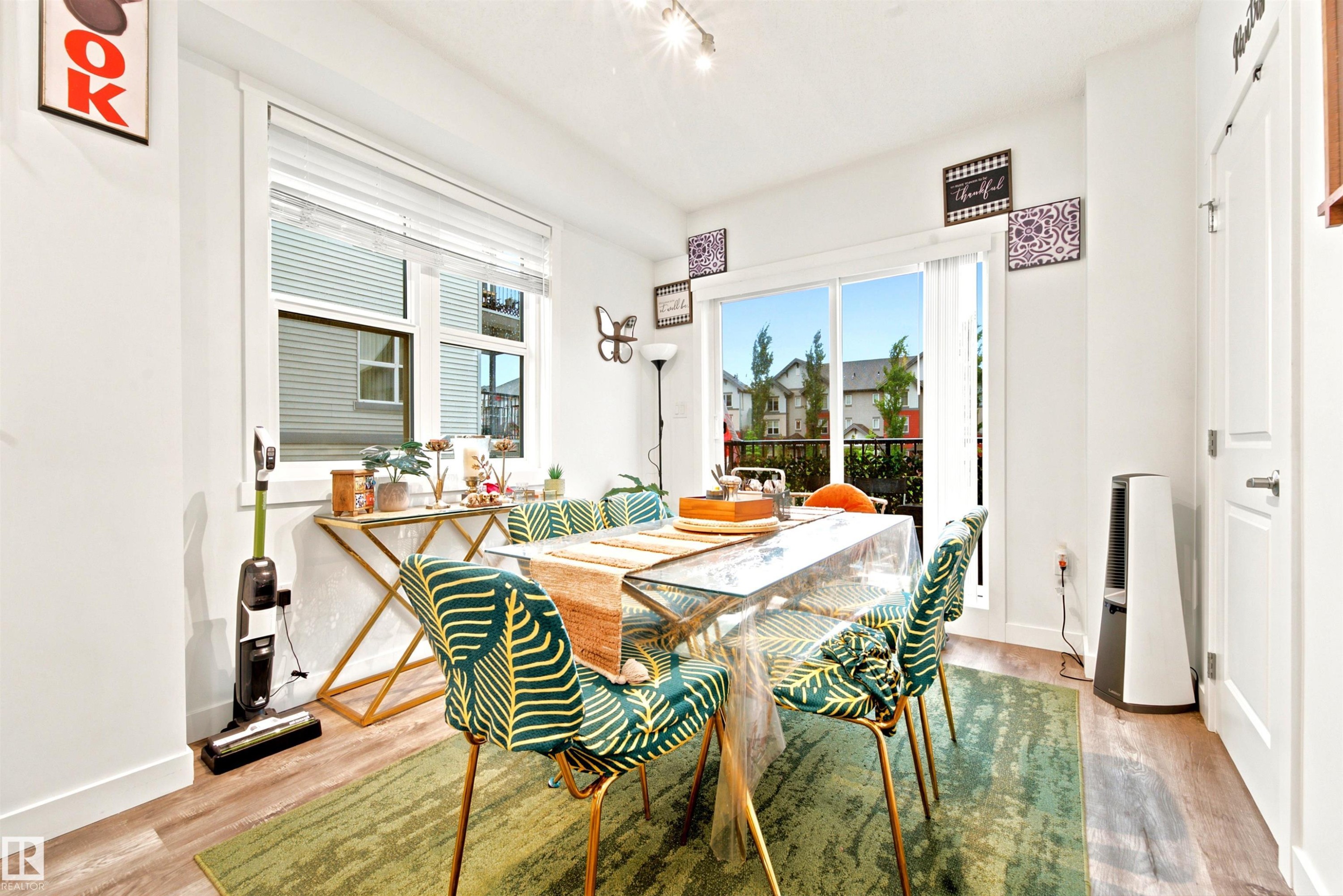Bright dining space featuring wood-finish flooring, a large window with blinds, and a glass sliding door providing access to an outdoor area - 64 655 Watt Boulevard, Edmonton, AB