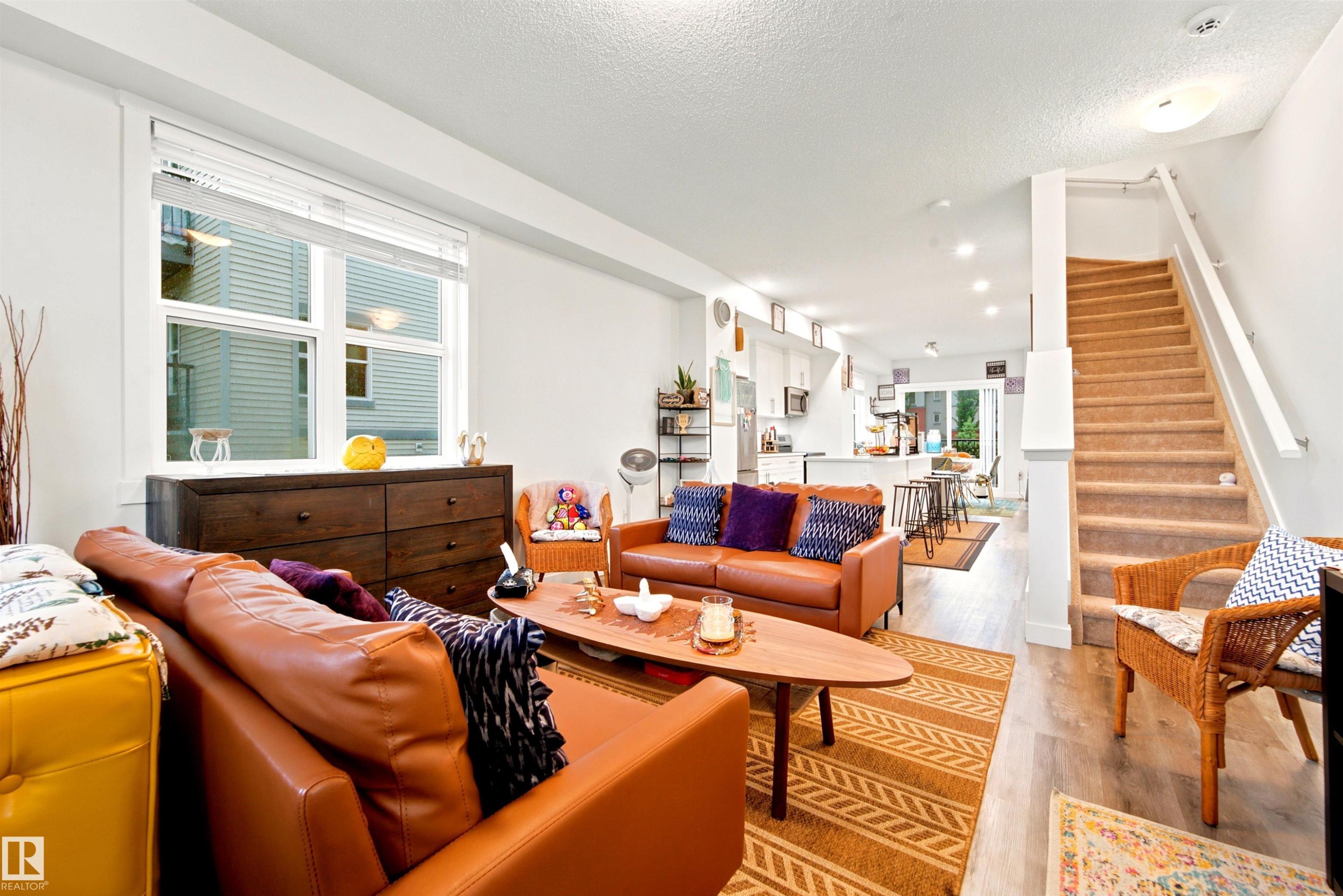 Open-concept living space featuring wood-finish flooring, a large window with blinds, recessed lighting, and a staircase with carpeting and a white handrail - 64 655 Watt Boulevard, Edmonton, AB