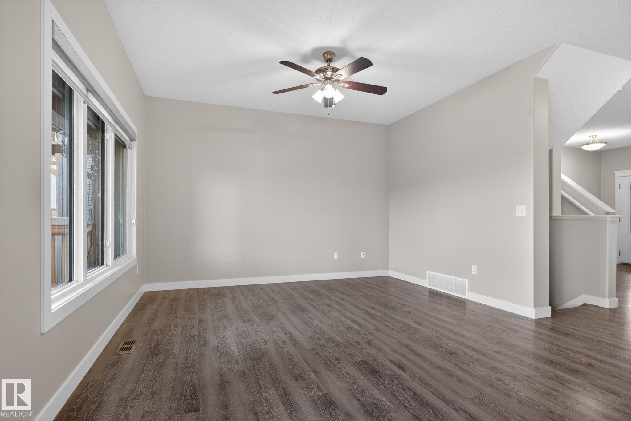 Spacious room featuring wood-finish flooring, a contemporary ceiling fan, and large windows providing ample natural light - 7341 Armour Crescent, Edmonton, AB - Indoor Photo Showing Other Room