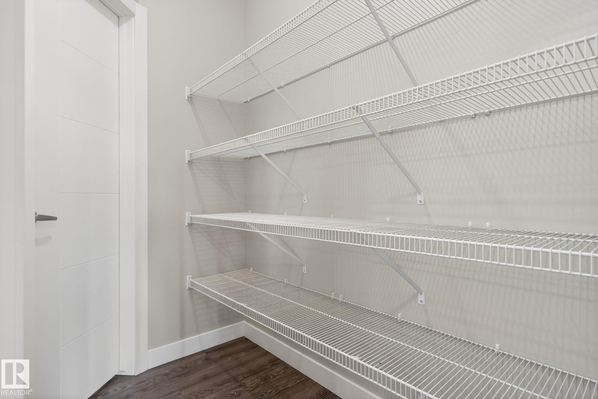 Spacious storage area featuring multiple tiers of white wire shelving, wood-finish flooring, and a contemporary paneled interior door - 7341 Armour Crescent, Edmonton, AB - Indoor With Storage