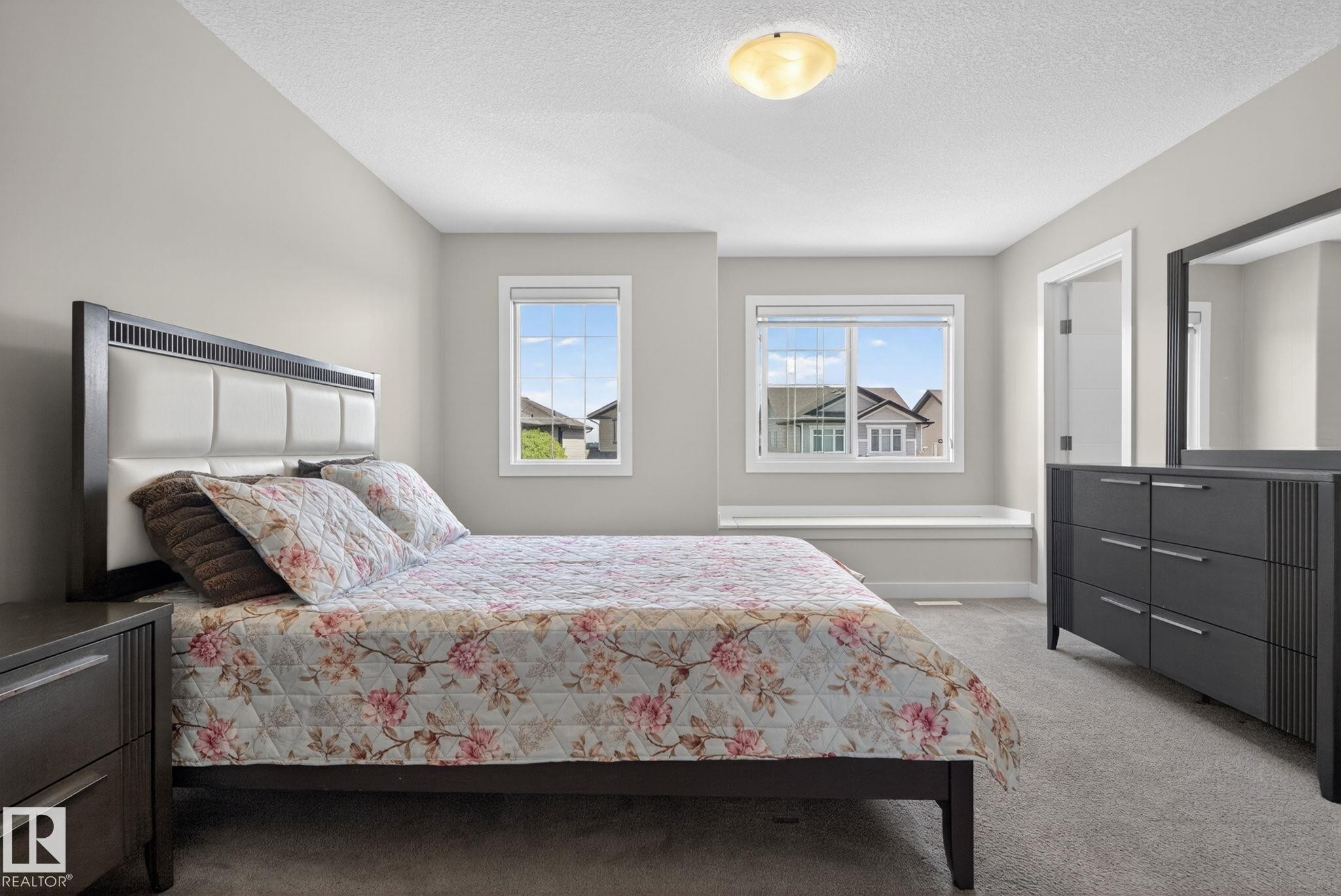 Carpeted bedroom featuring two windows with white trim, a built-in window bench, a flush-mount ceiling light, and light gray wall paint - 7341 Armour Crescent, Edmonton, AB - Indoor Photo Showing Bedroom