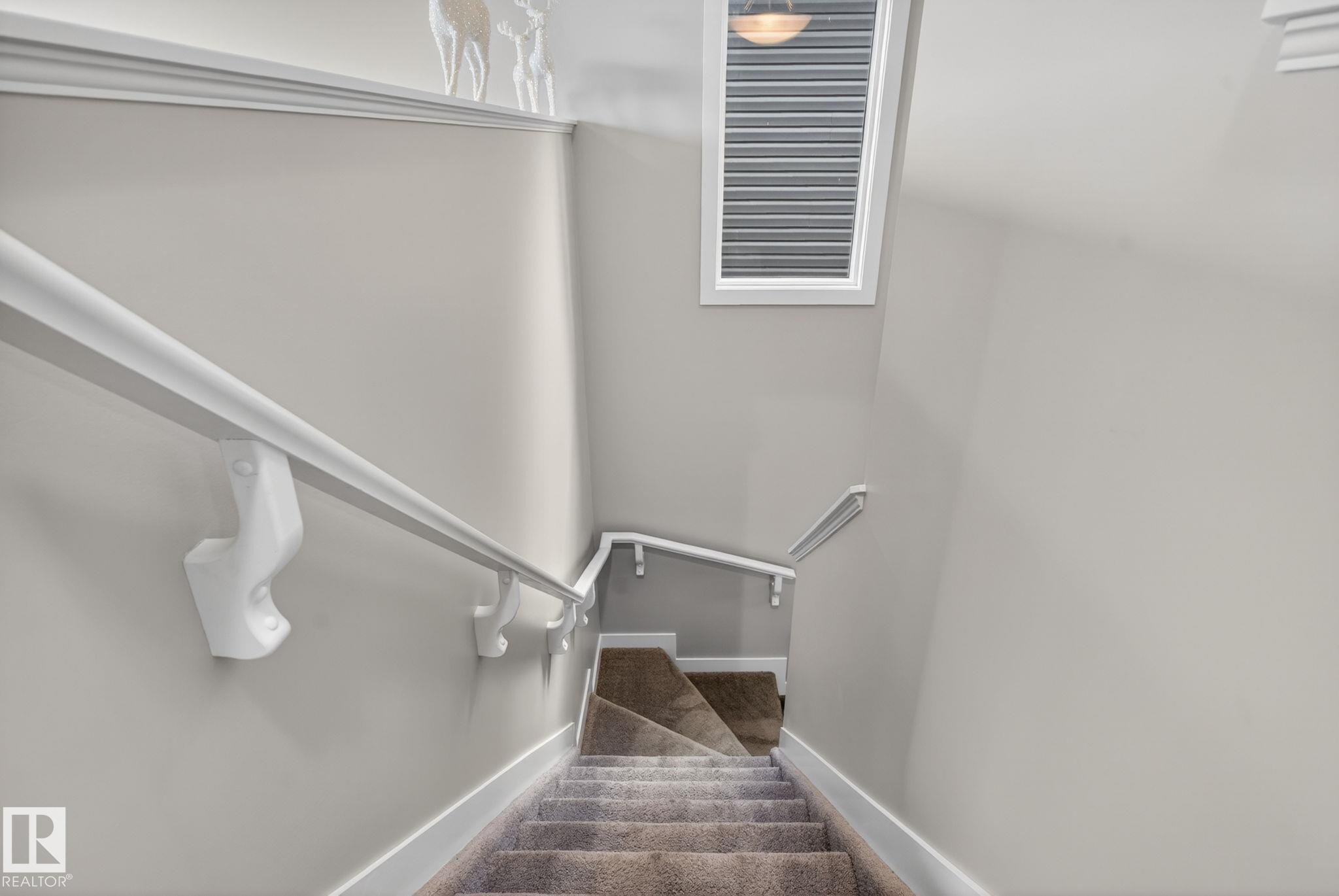 Carpeted staircase featuring white handrails, white baseboards, and light gray wall paint - 7341 Armour Crescent, Edmonton, AB - Indoor Photo Showing Other Room