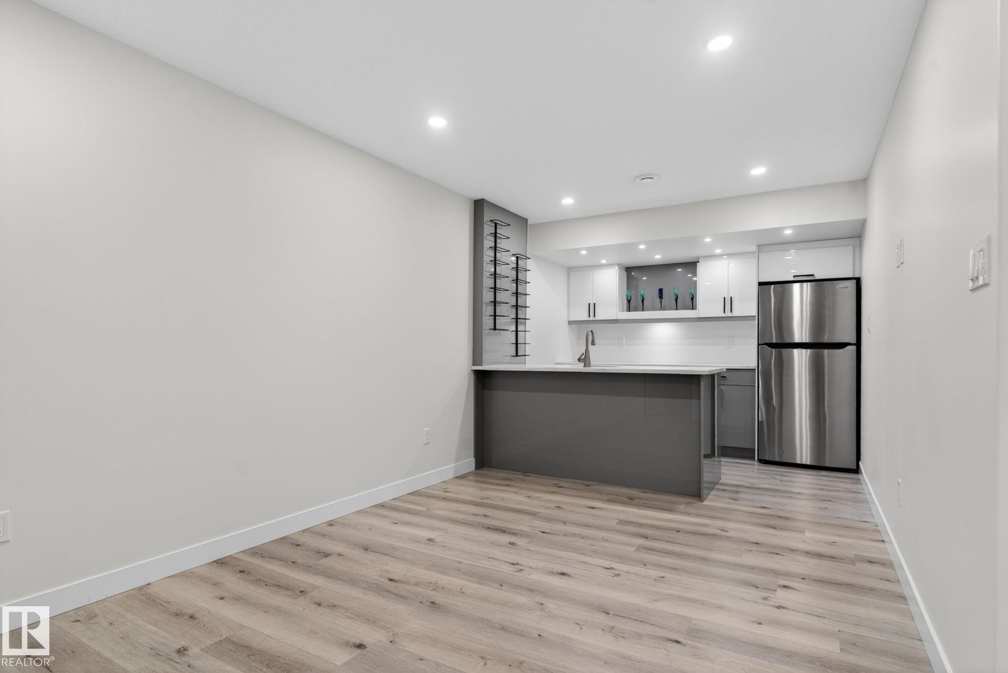 Compact kitchen area featuring a stainless steel refrigerator, white cabinetry, and a light-toned countertop - 7341 Armour Crescent, Edmonton, AB - Indoor