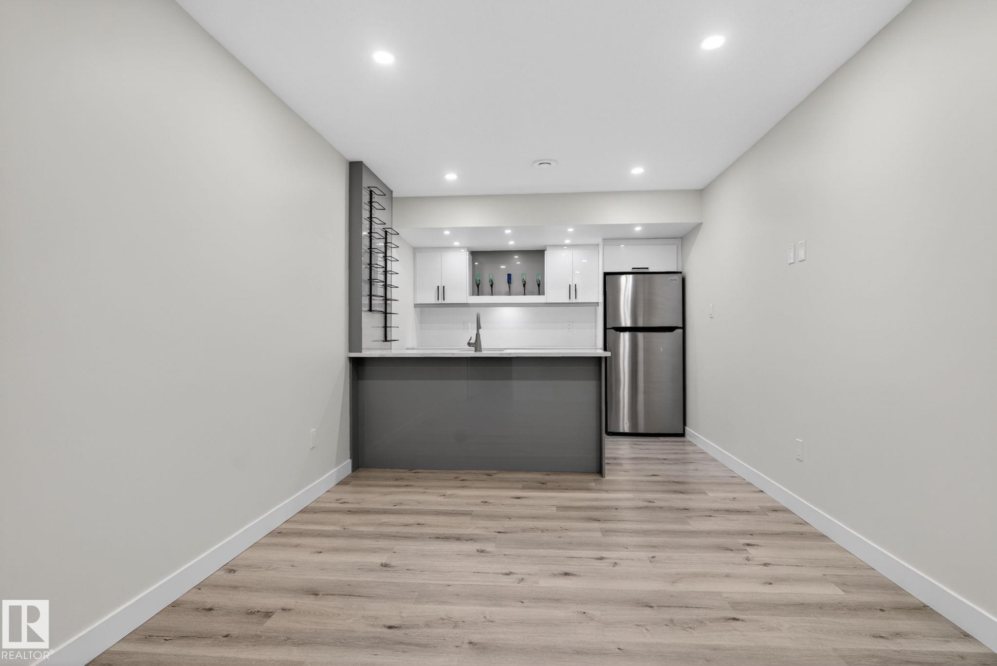 Compact kitchen featuring a stainless steel refrigerator, white cabinetry, integrated sink, and gray island with countertop seating - 7341 Armour Crescent, Edmonton, AB - Indoor Photo Showing Other Room