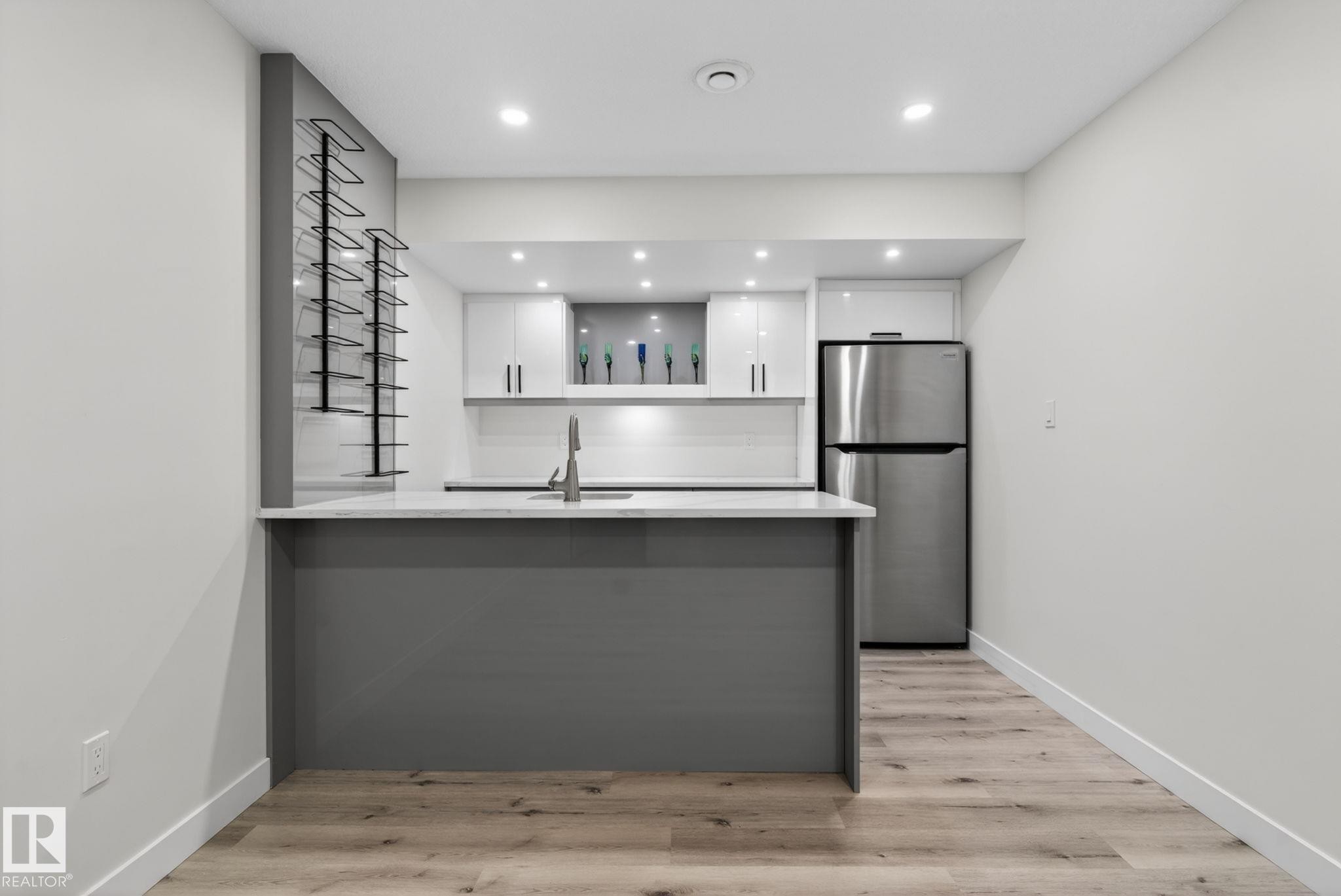 Modern kitchen featuring a gray island with a white countertop, stainless steel appliances, recessed lighting, white cabinetry, and wood-finish flooring - 7341 Armour Crescent, Edmonton, AB - Indoor