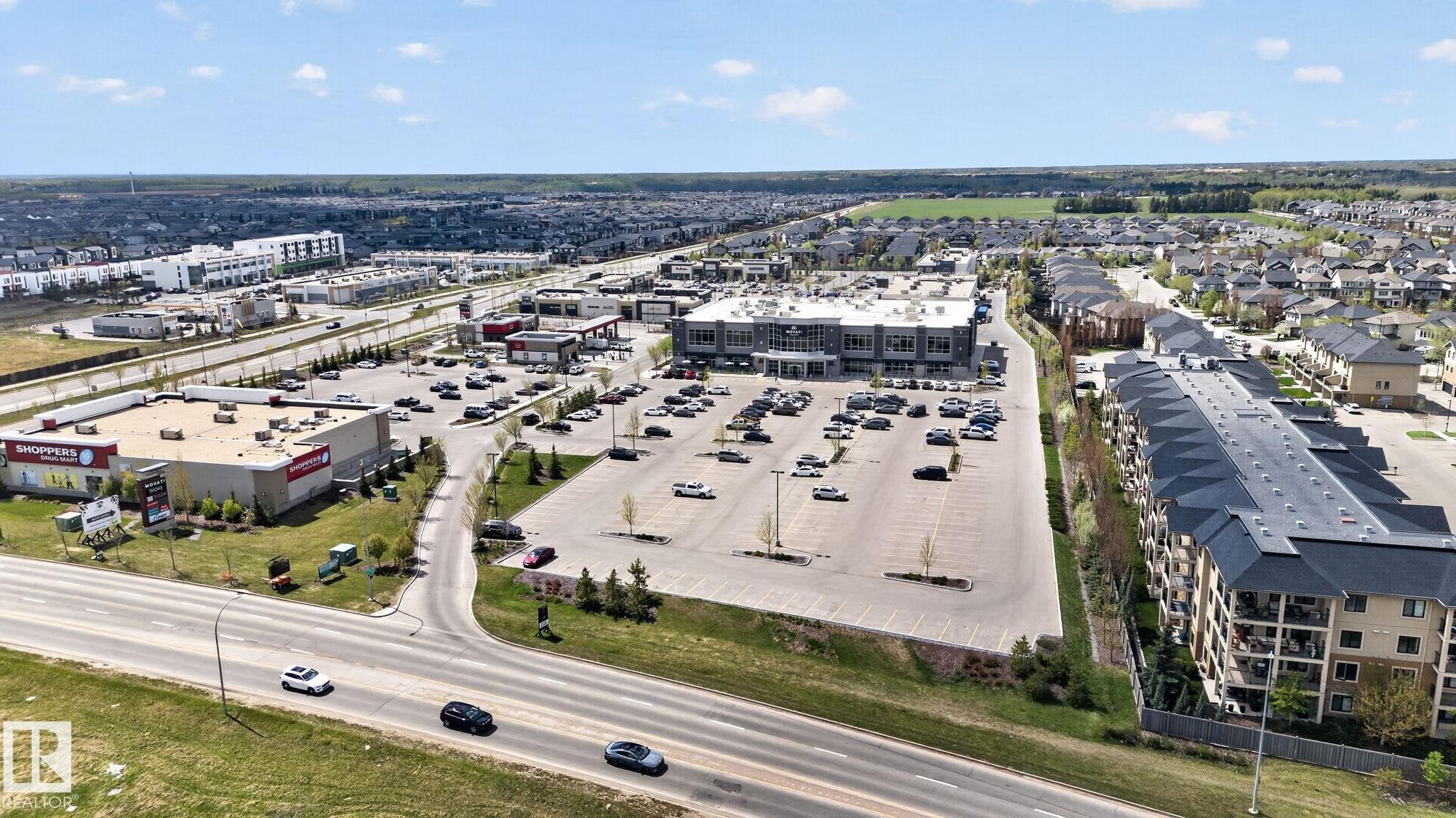 Aerial perspective showcasing a mixed-use development with commercial buildings, extensive surface parking, and multi-story residential structures - 7341 Armour Crescent, Edmonton, AB - Outdoor With View