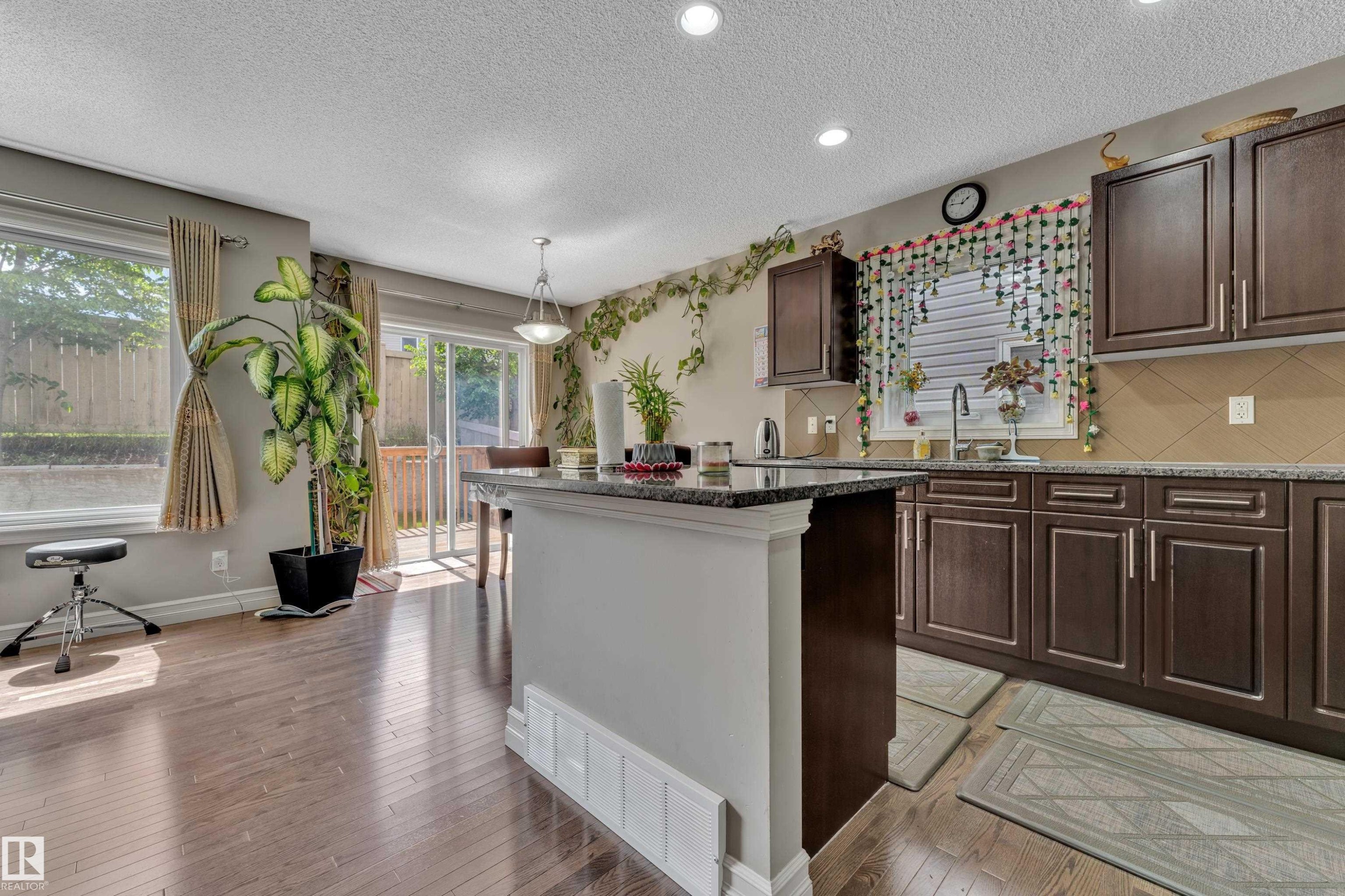 Kitchen featuring dark wood-finish cabinetry, a large center island with a dark countertop, and a tile backsplash - #24 655 Tamarck Rd Nw, Edmonton, AB - Indoor Photo Showing Kitchen With Upgraded Kitchen