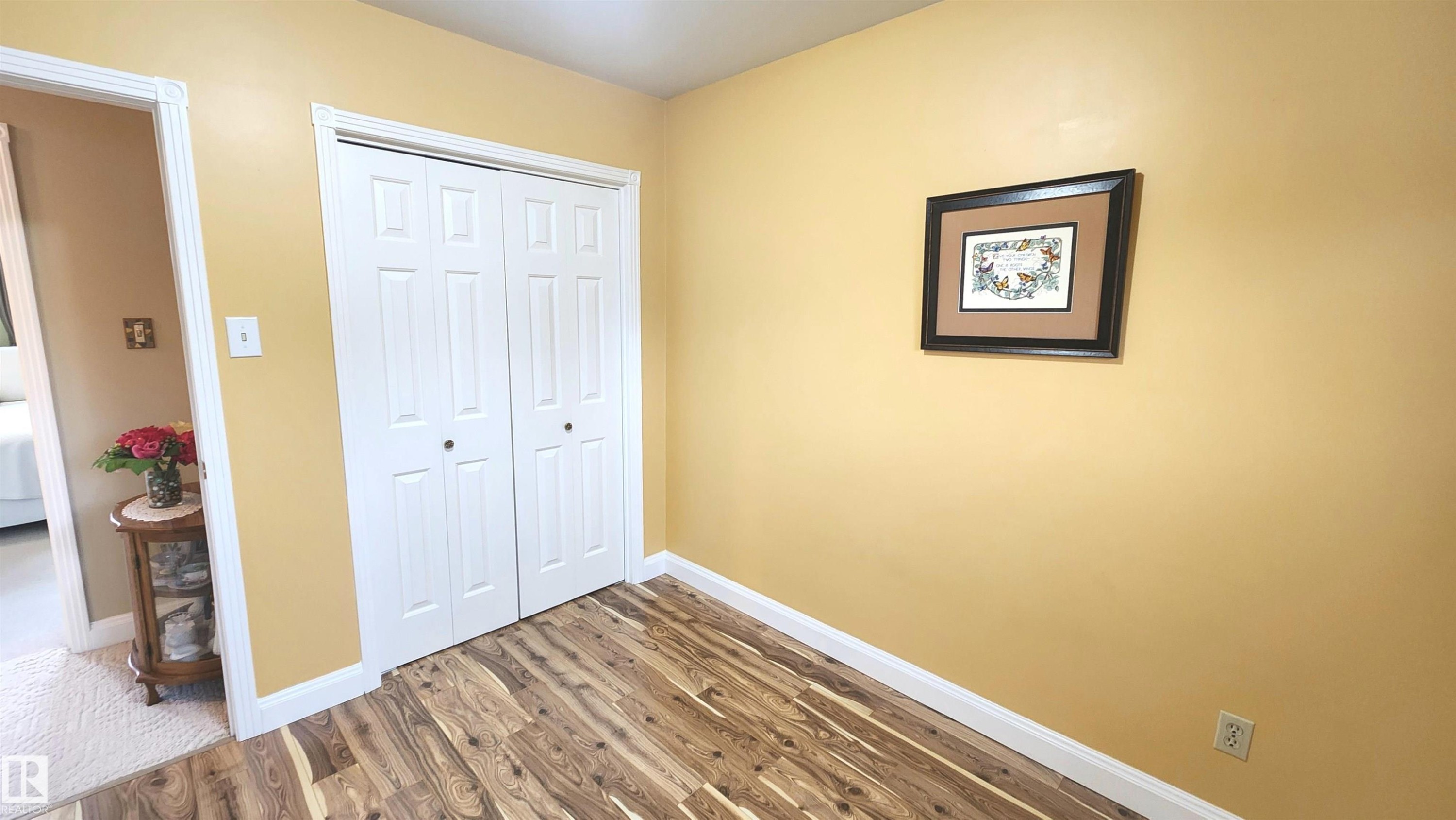 Room featuring wood-finish flooring, white baseboards, and a bi-fold closet with panel doors - 13307 Delwood Road, Edmonton, AB