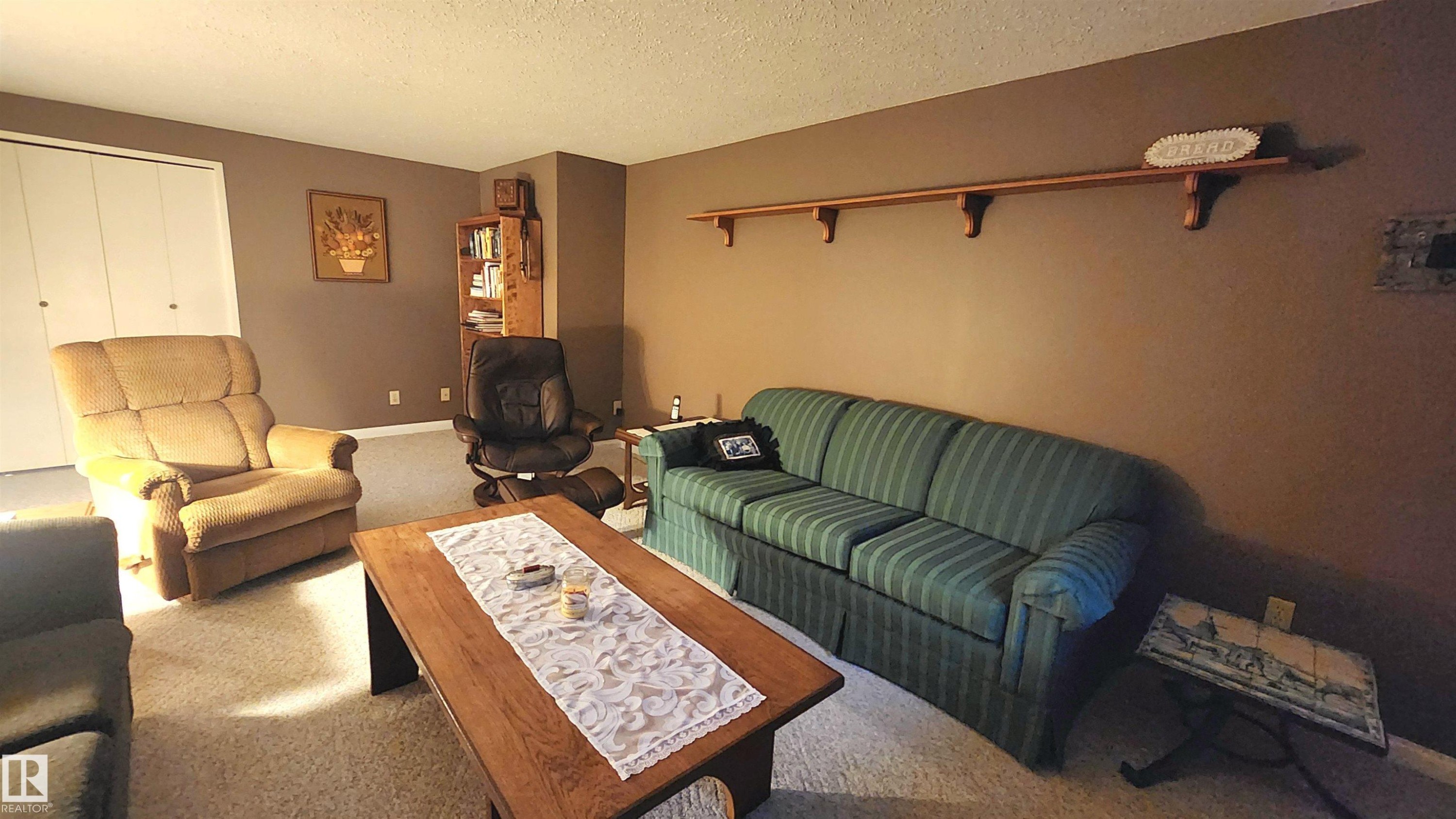 Carpeted living area featuring a built-in wooden shelving unit, neutral wall tones, and a white bi-fold closet - 13307 Delwood Road, Edmonton, AB