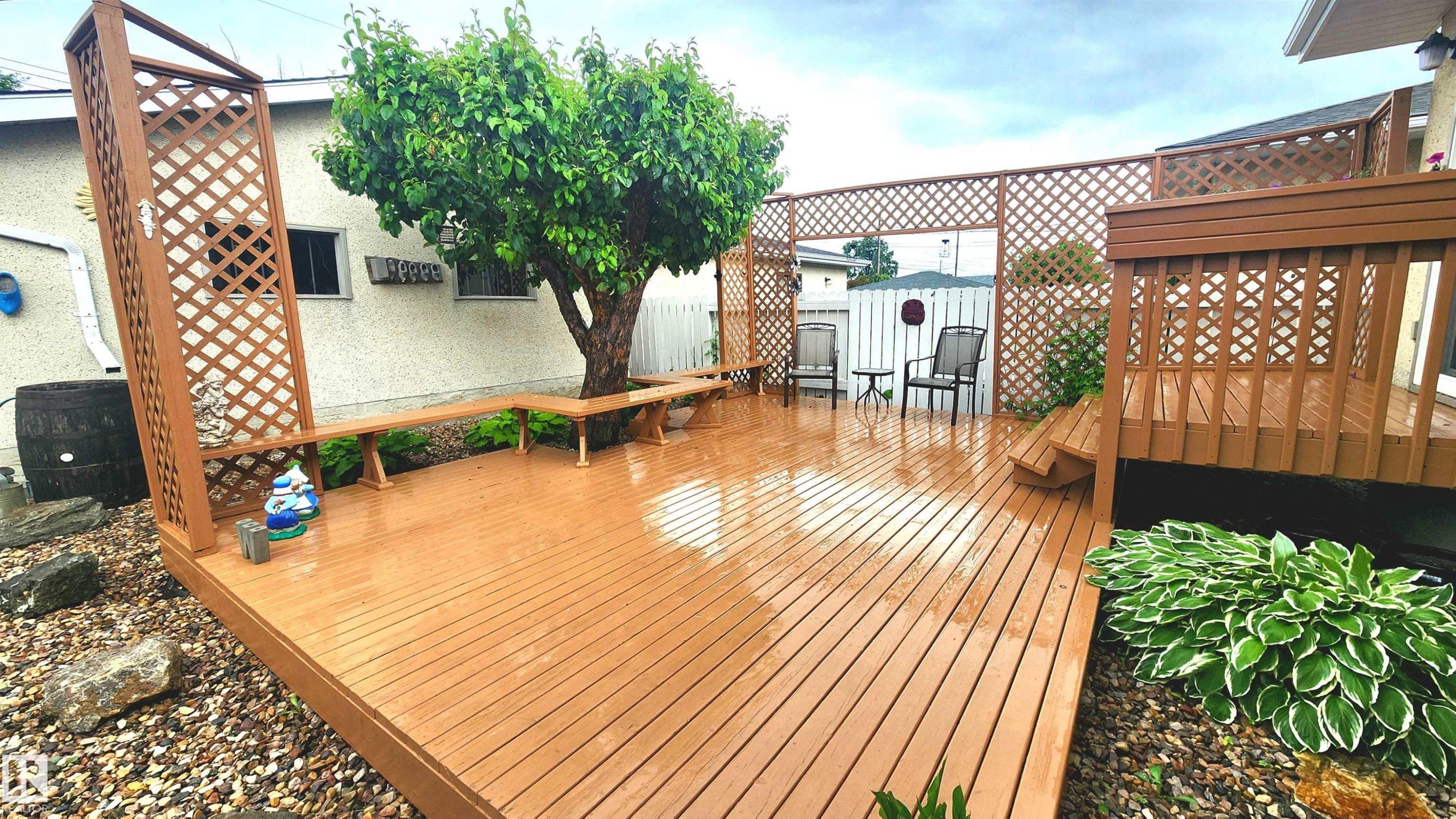 Expansive wood-finish deck featuring built-in perimeter seating, a built-in privacy screen with lattice detailing, and mature plantings - 13307 Delwood Road, Edmonton, AB